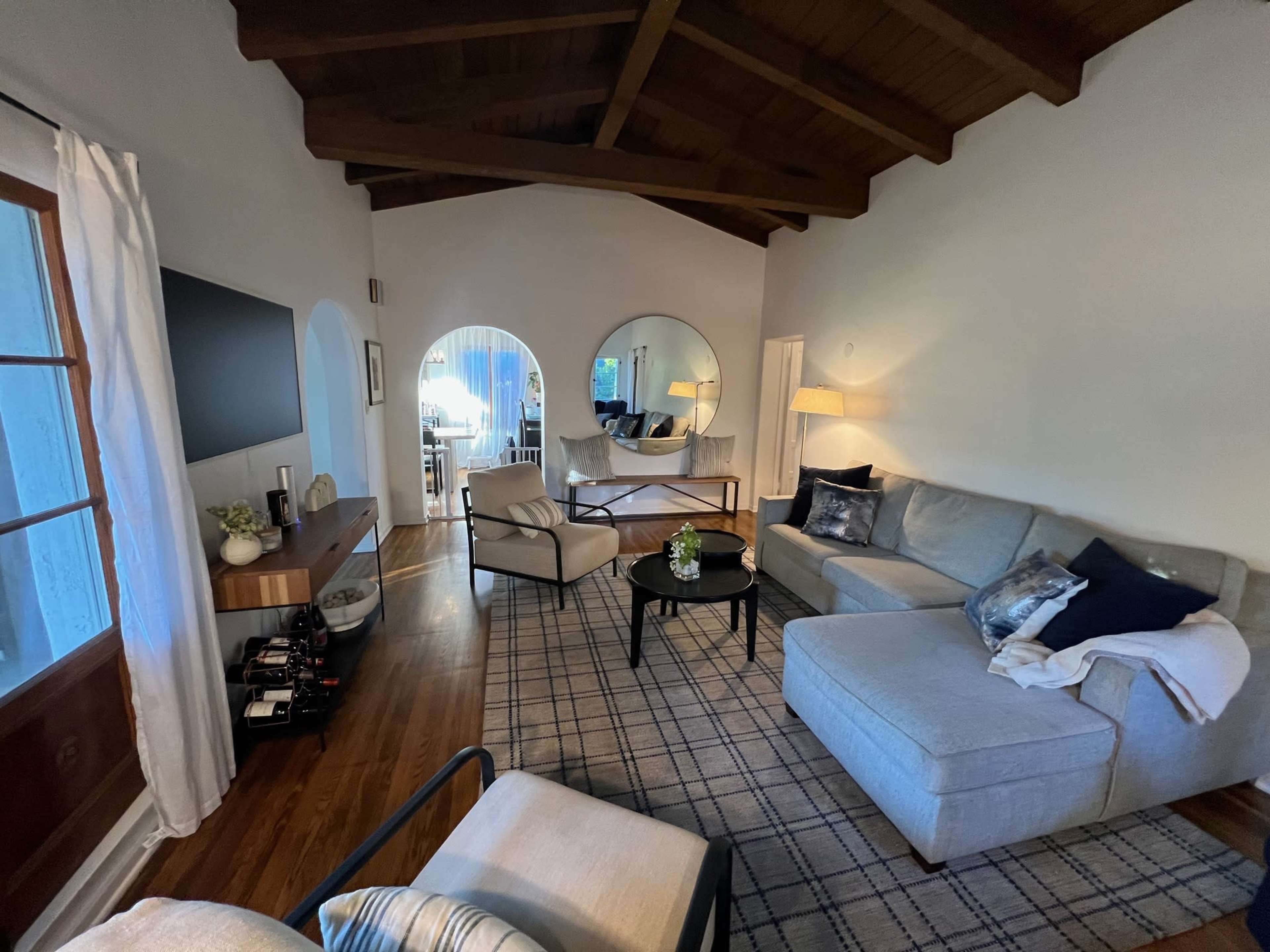 The image shows a spacious living room with a large sectional sofa, a round coffee table, and a wooden ceiling.
