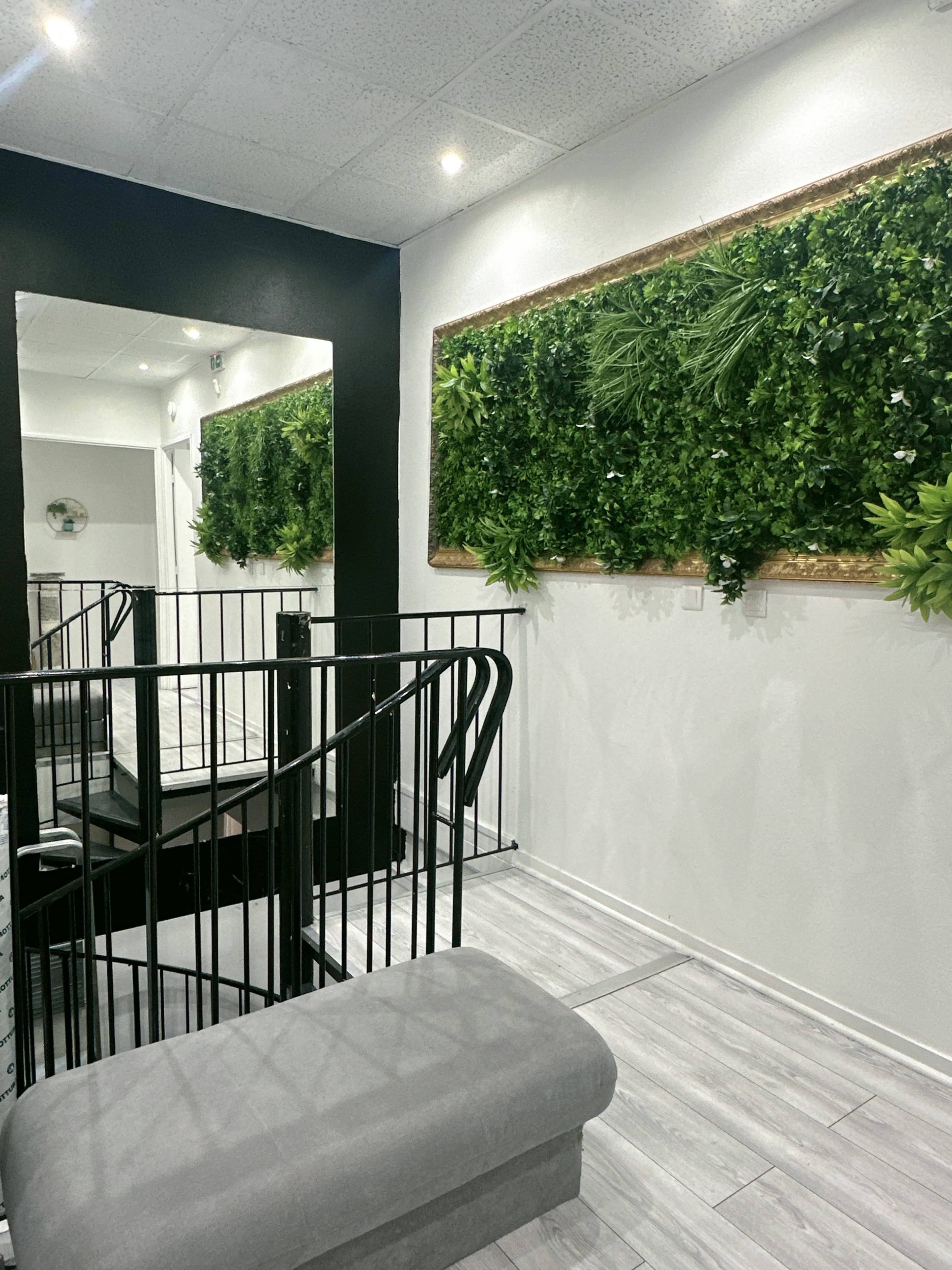 A modern stairwell with a black and white color scheme, featuring a wall of greenery and a large mirror.