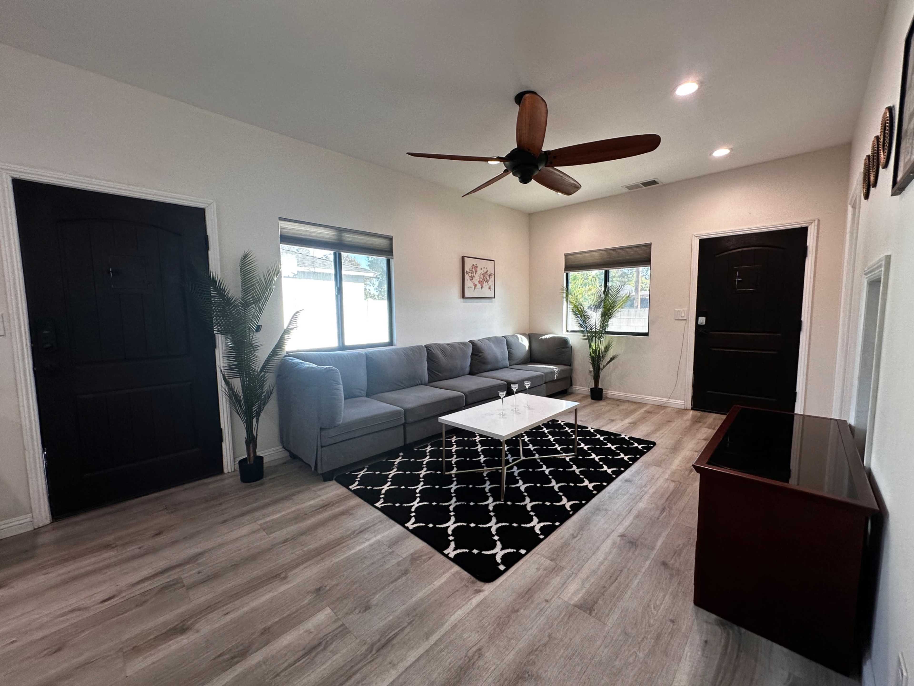 The living room features a gray sectional sofa, a black and white patterned rug, a coffee table, and two windows with natural light.