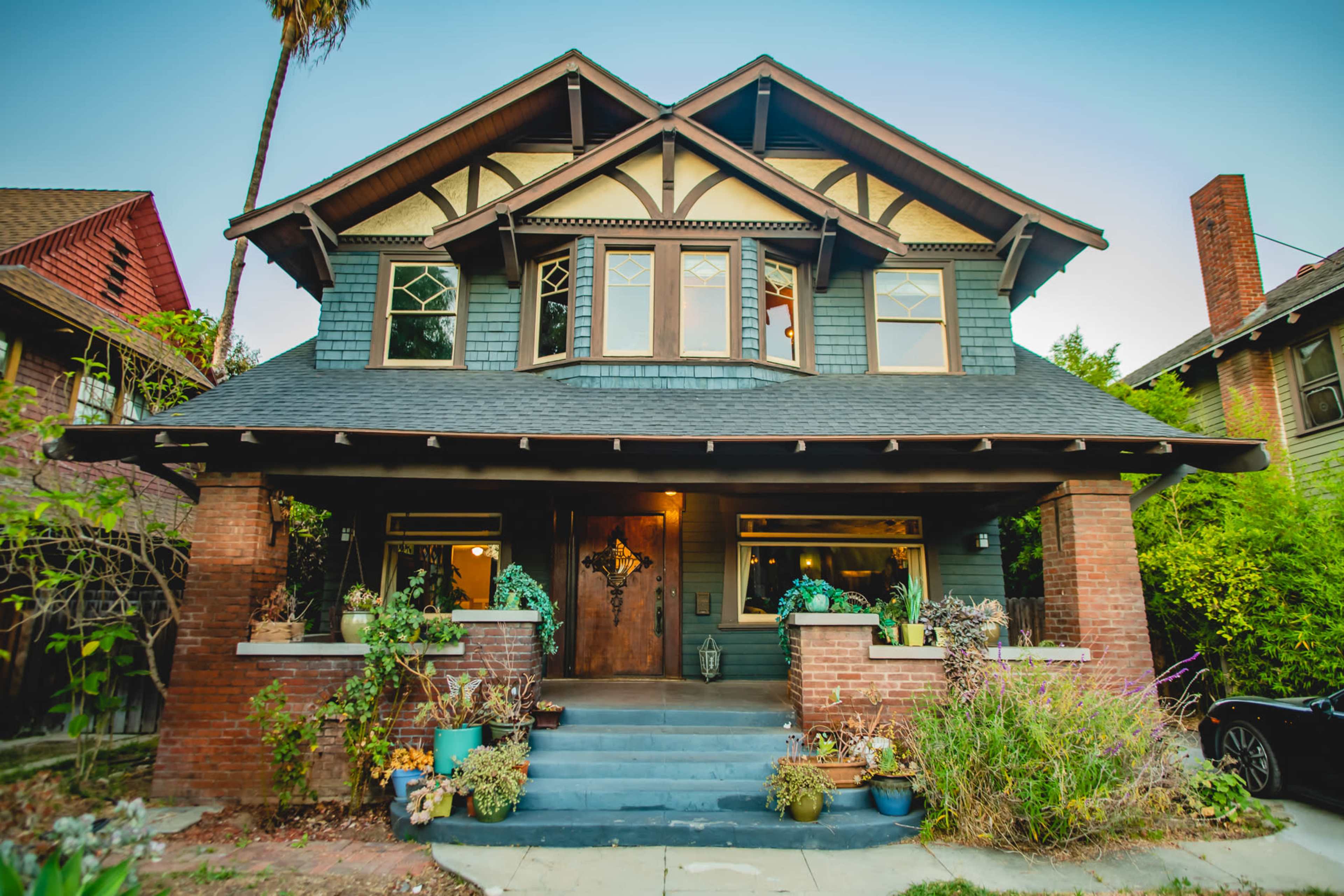 A large two-story Craftsman-style house with a front porch, surrounded by various plants and trees.