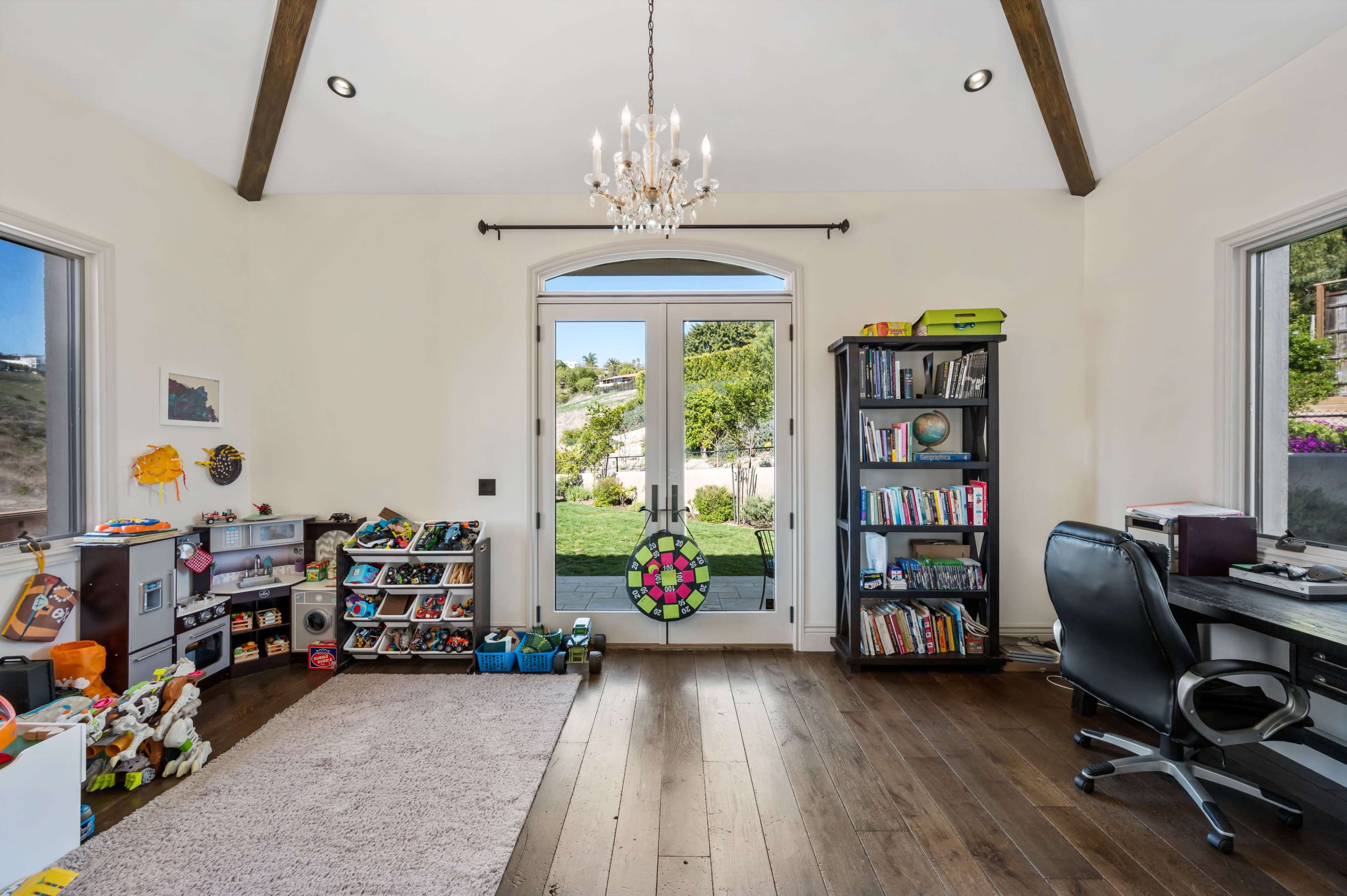 A well-lit room features a door leading to an outdoor area, bookshelves filled with books, and storage for shoes and toys.