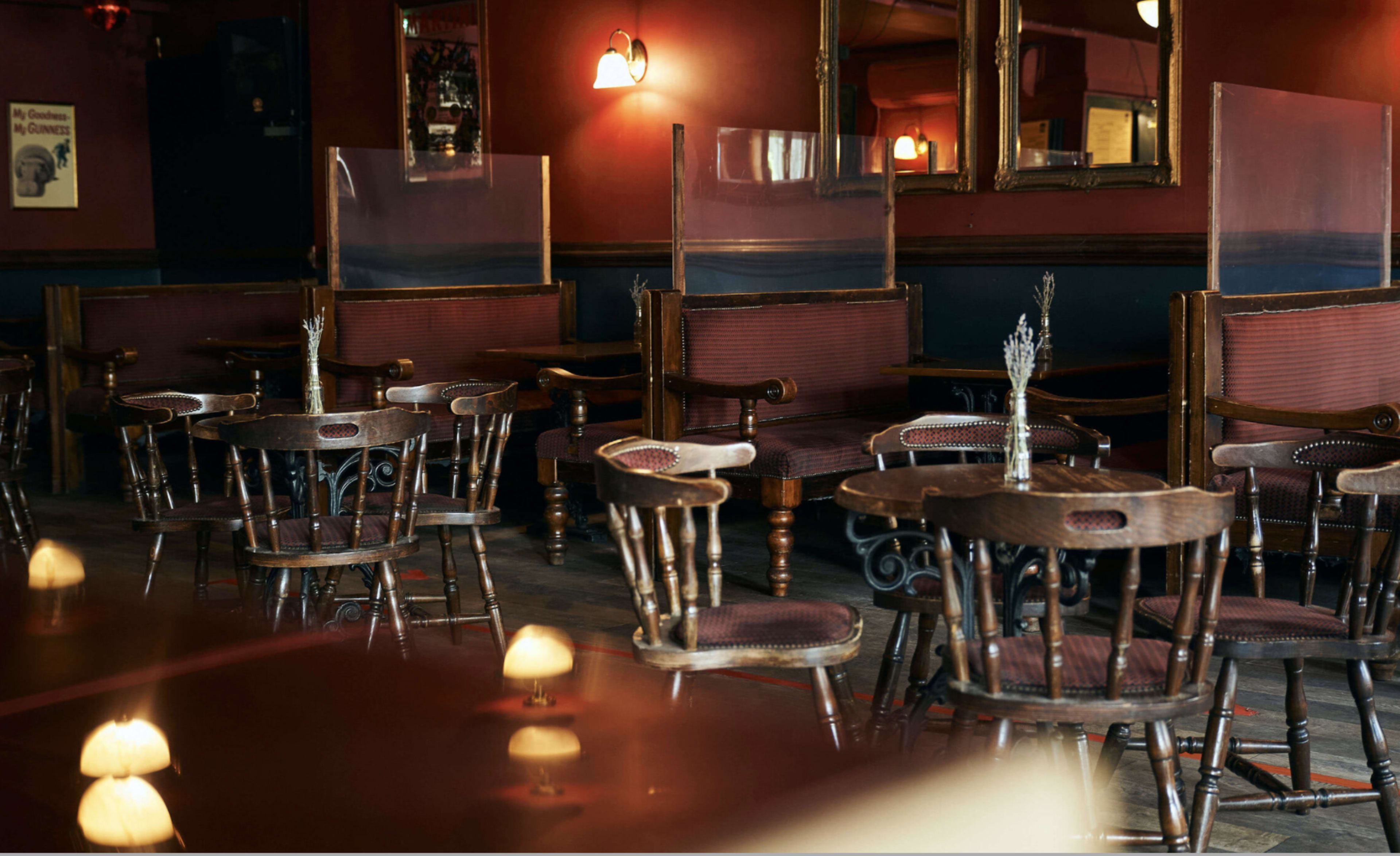 A dimly lit restaurant with wooden tables and chairs arranged in an intimate setting, separated by transparent dividers.
