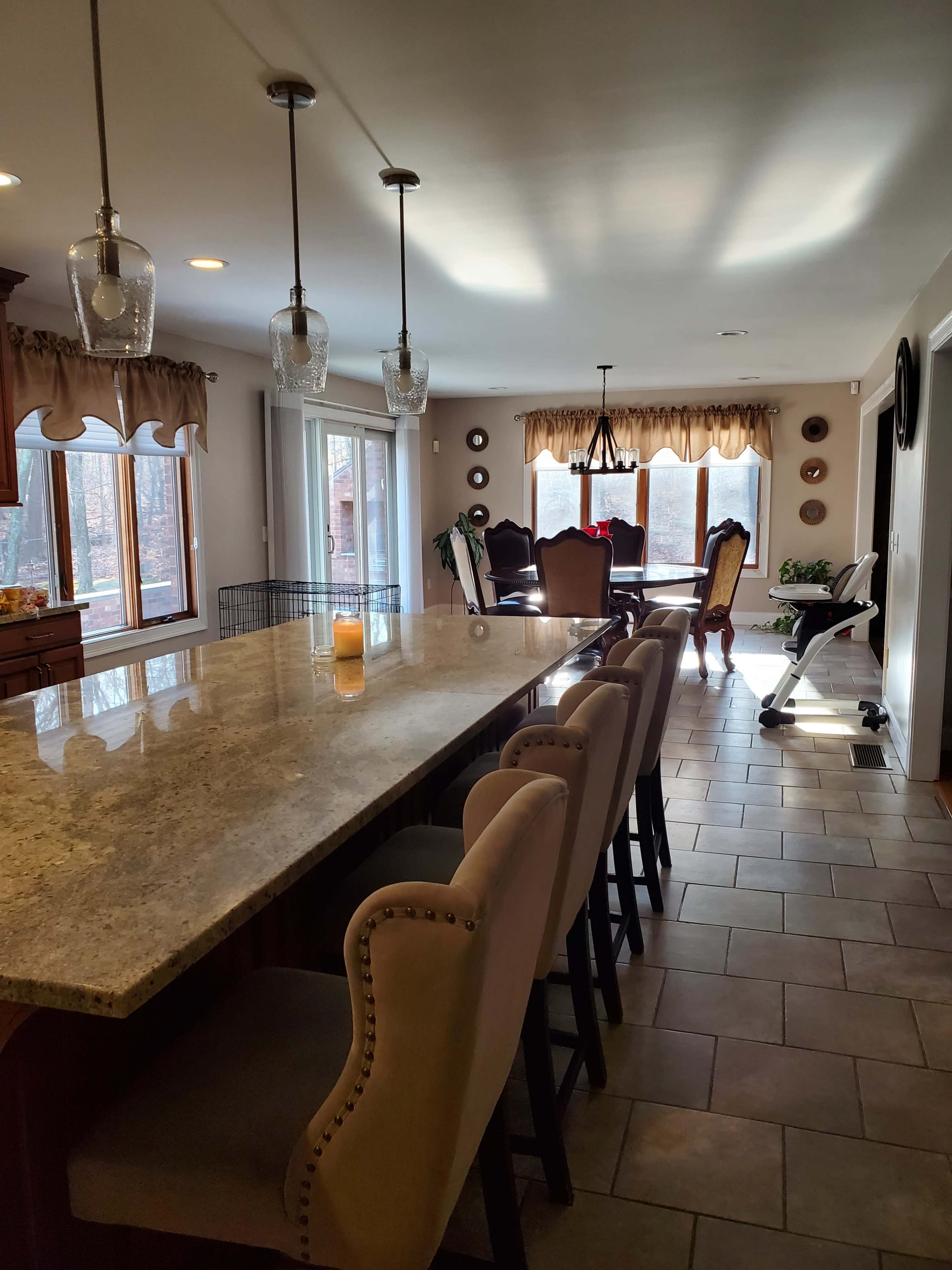 A spacious kitchen with a granite island featuring seating, facing an adjacent dining area with large windows and a polished wooden table.