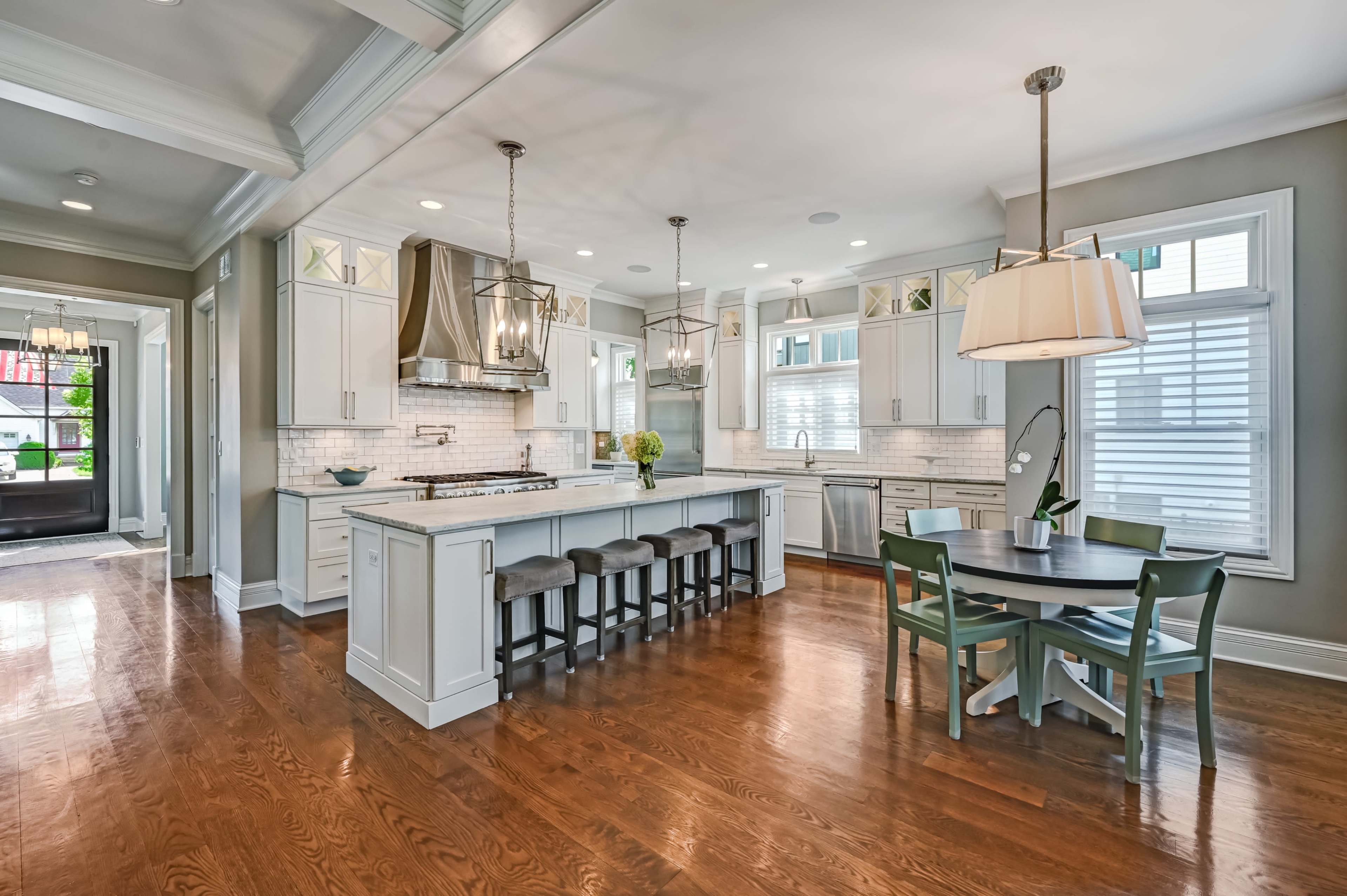The image shows a modern kitchen and dining area with a large island, pendant lighting, and dining table set against a backdrop of hardwood flooring.