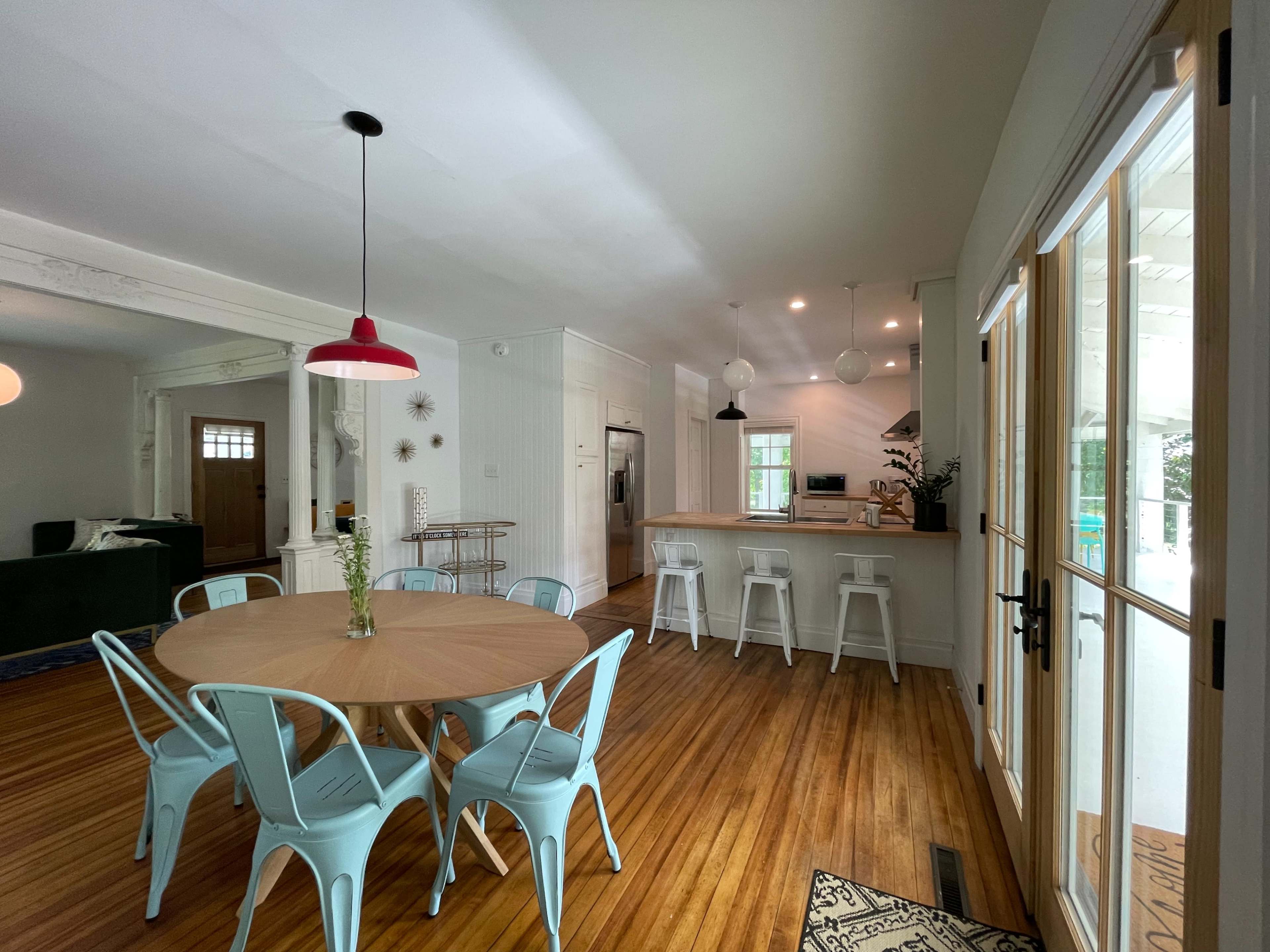 A dining area features a round wooden table surrounded by light blue chairs, with an open kitchen visible in the background.