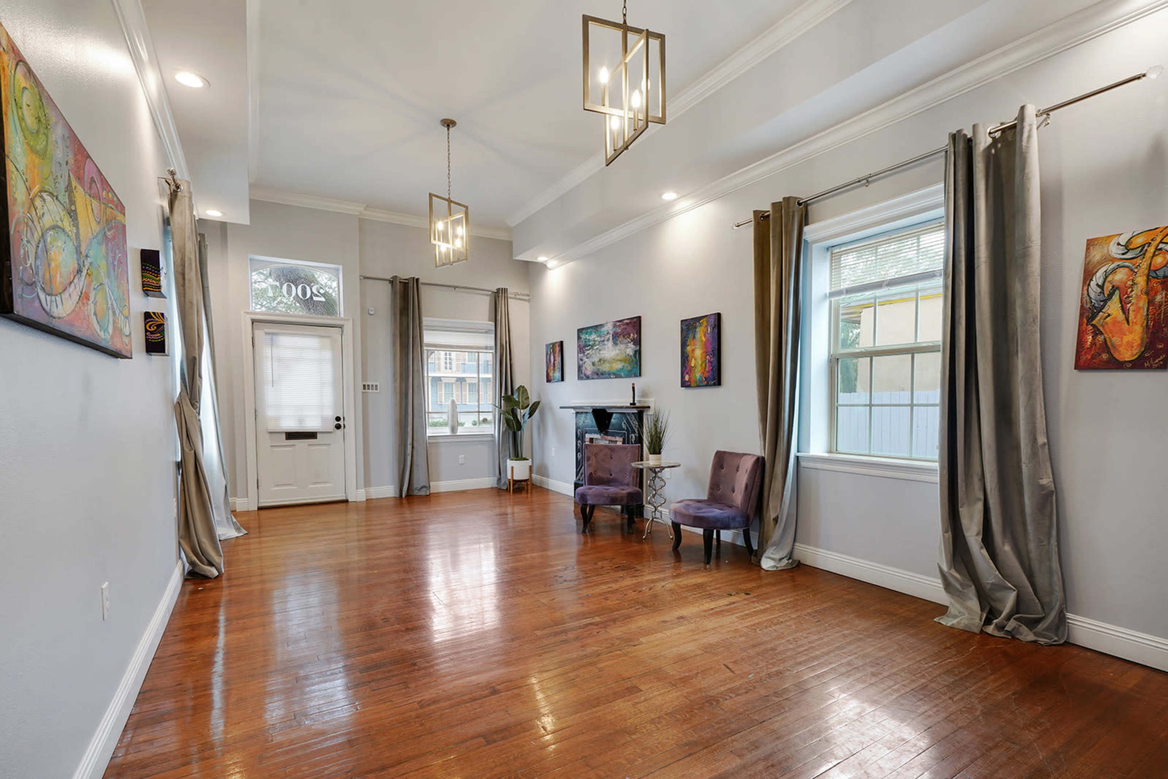 A spacious interior room features wooden flooring, light-colored walls, decorative artwork, and two chairs near a window.