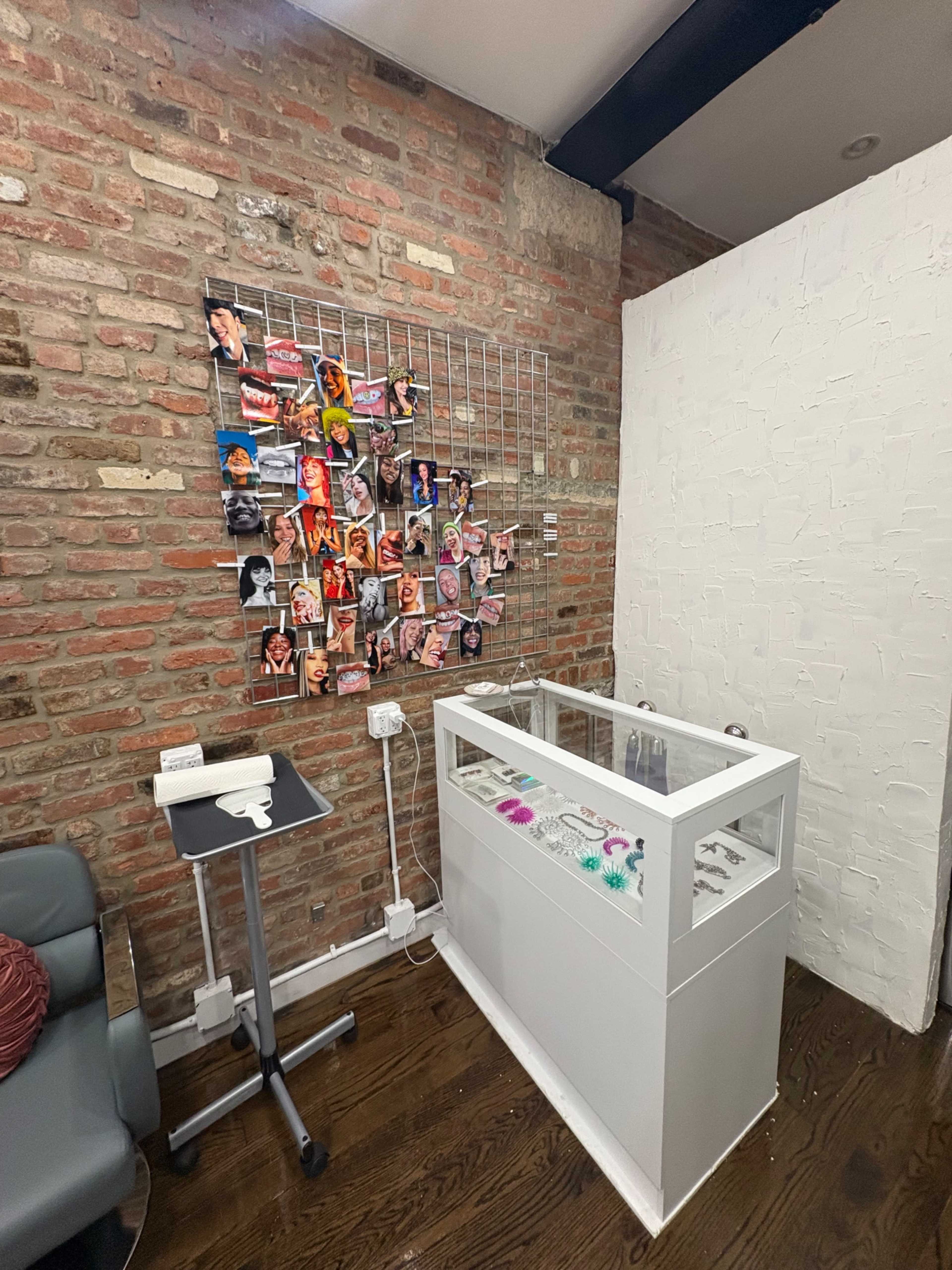The image shows a contemporary room with a brick wall featuring a collage of photographs, a display case for products, and a small table with a clipboard.
