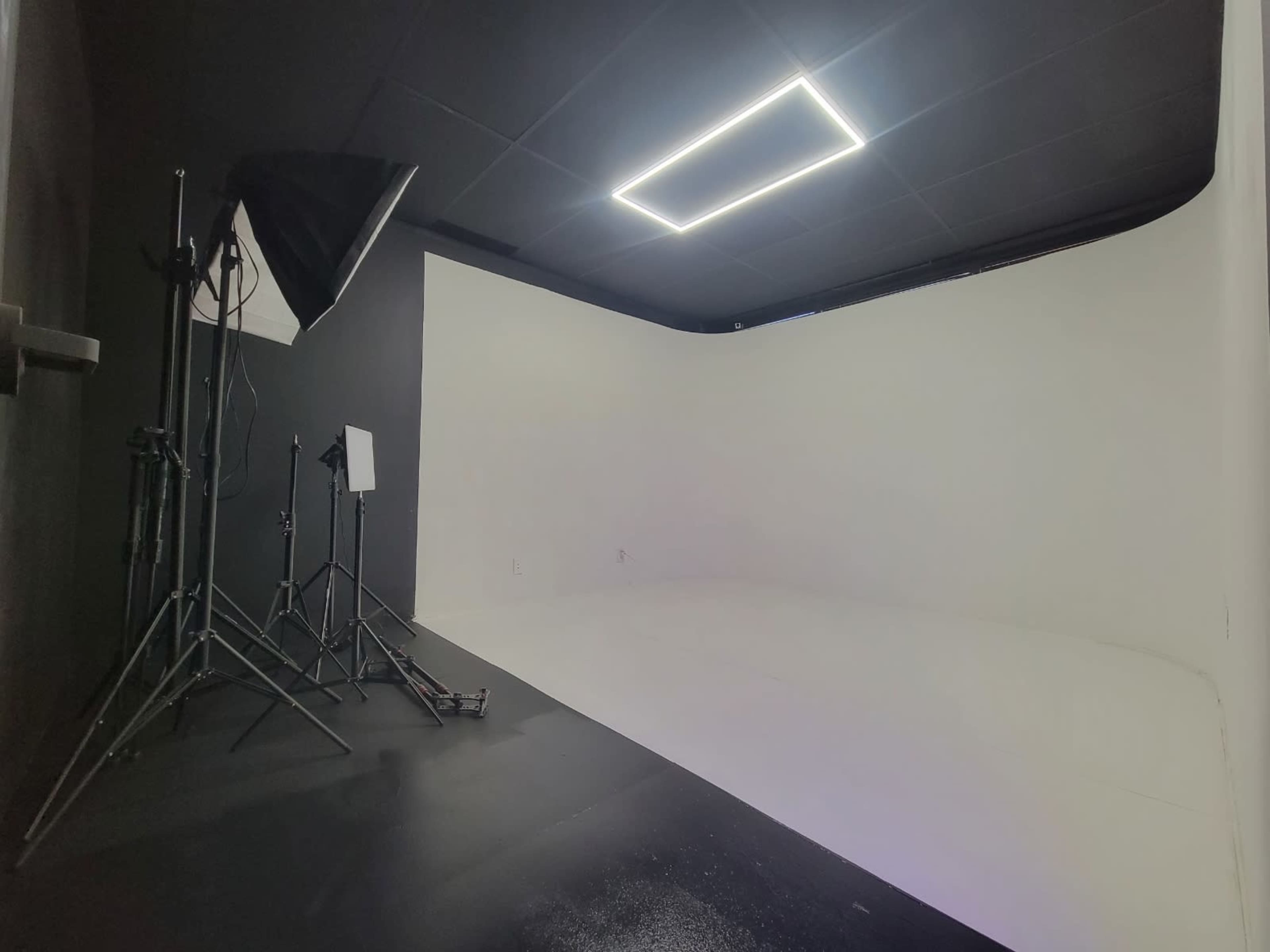 The image shows a photography studio with a seamless white backdrop, lighting equipment, and a clean black floor.