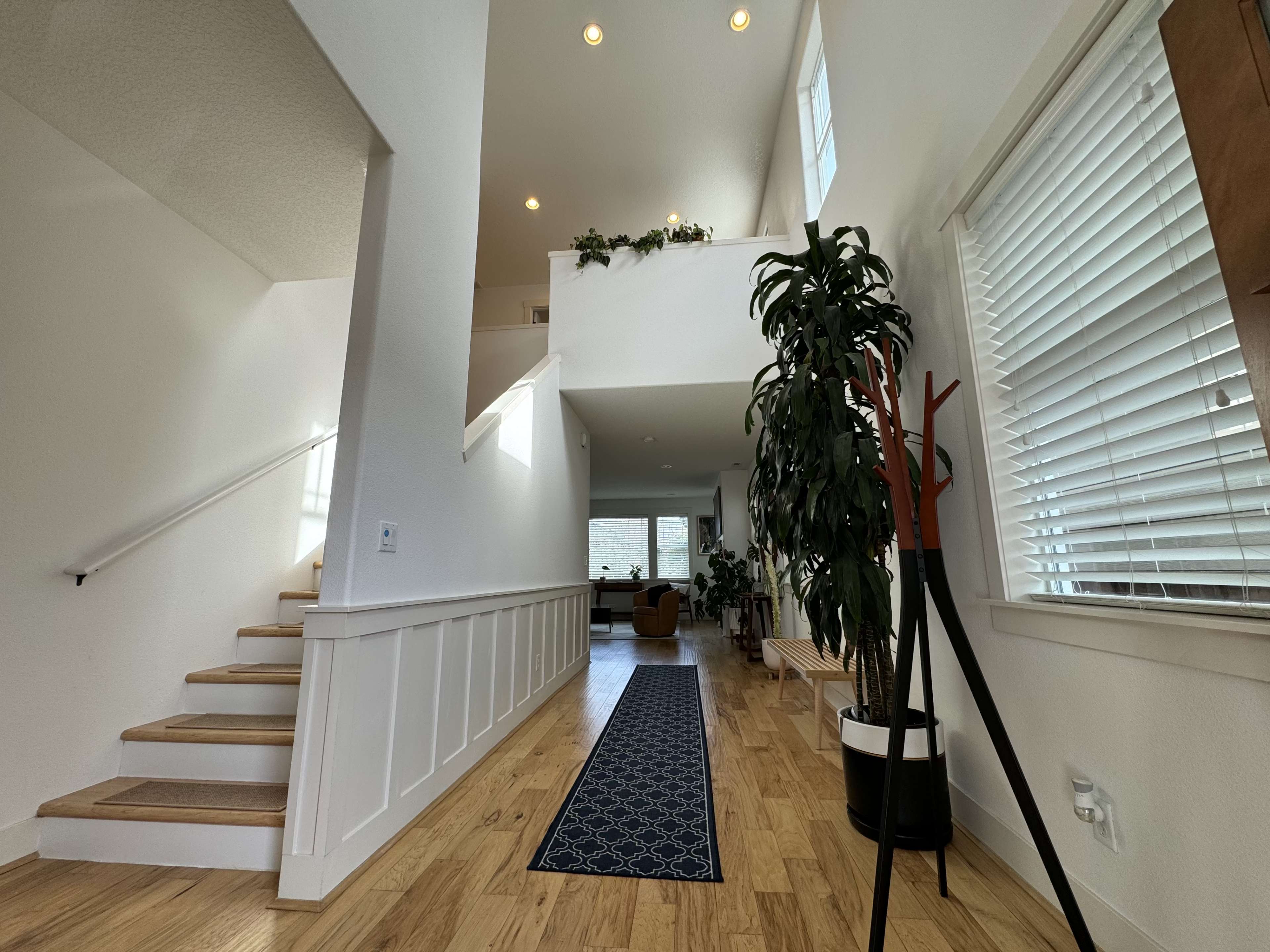 A spacious, modern hallway with wooden stairs, a runner rug, and large windows that allow natural light to illuminate the space.