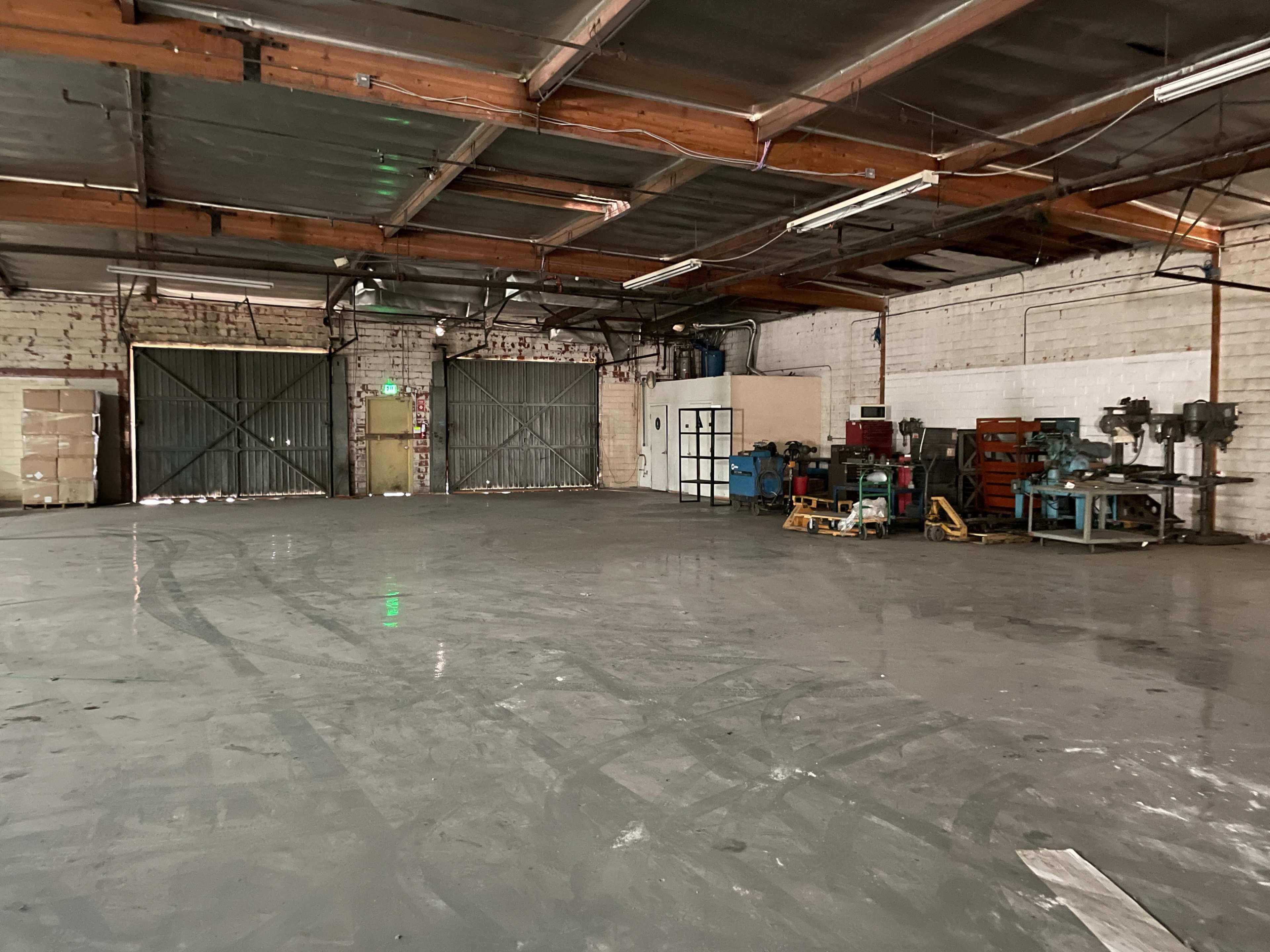 A spacious warehouse interior features concrete flooring, exposed beams, and various industrial equipment along one side.