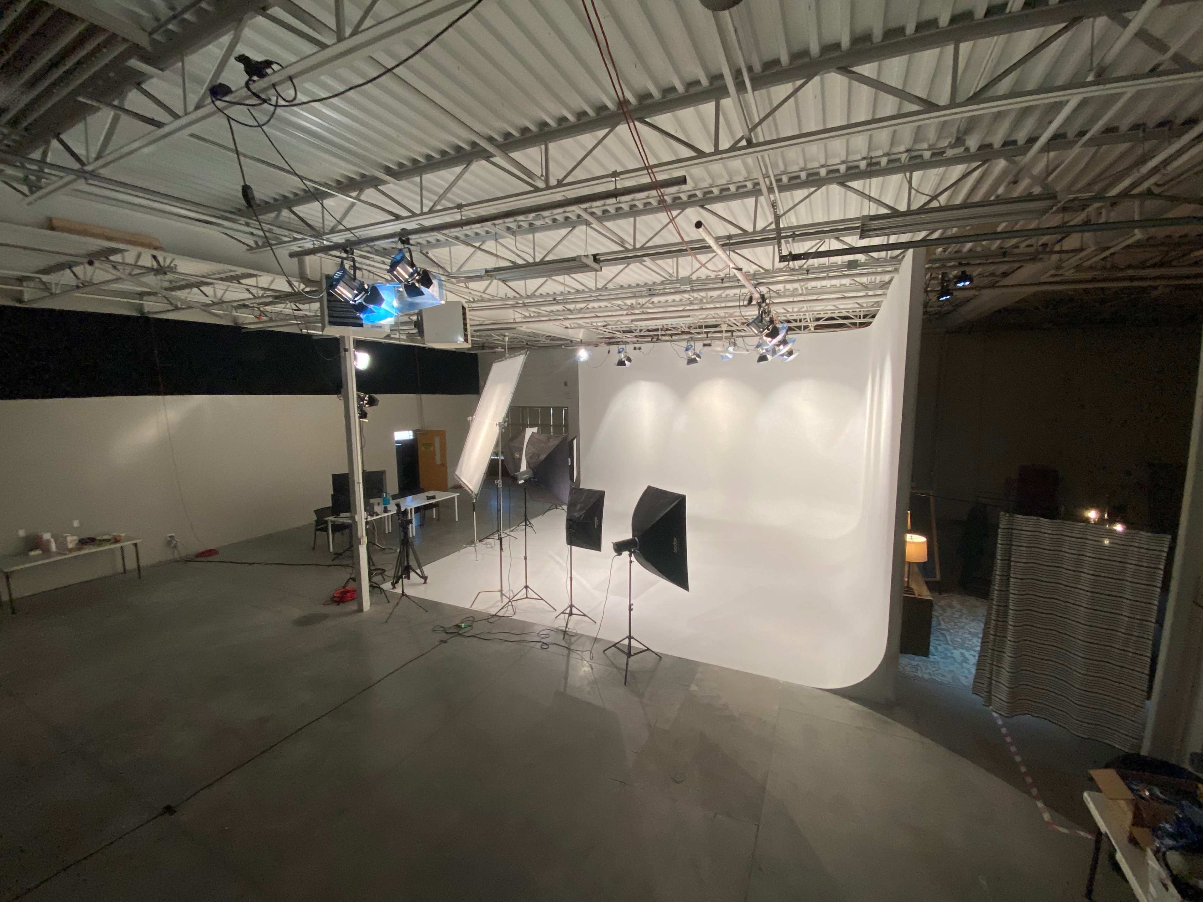 A photography studio with a white backdrop, softbox lighting setup, and various equipment arranged on the floor.