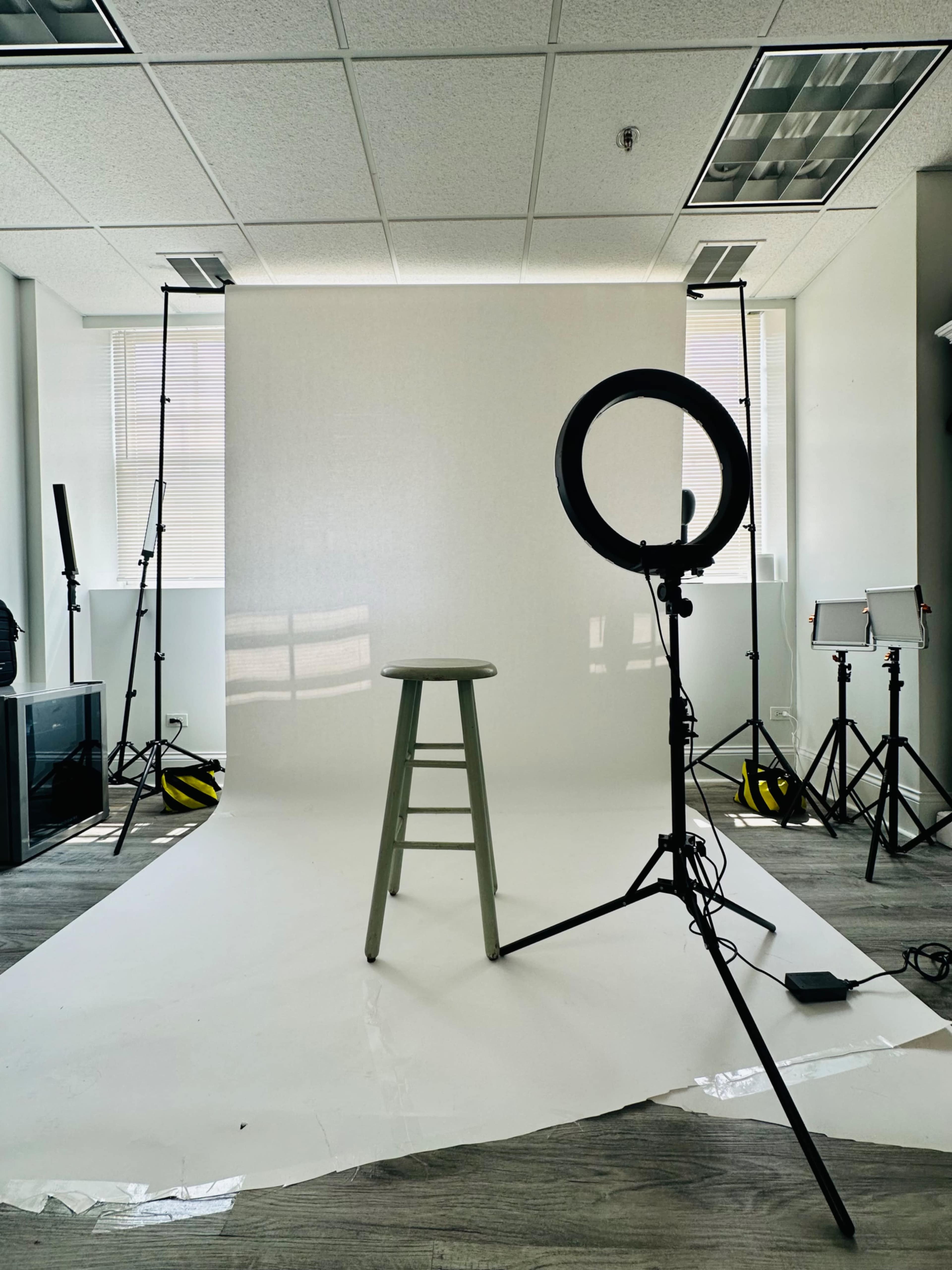 The image shows a photography studio setup with a green stool on a white backdrop surrounded by lighting equipment and tripods.