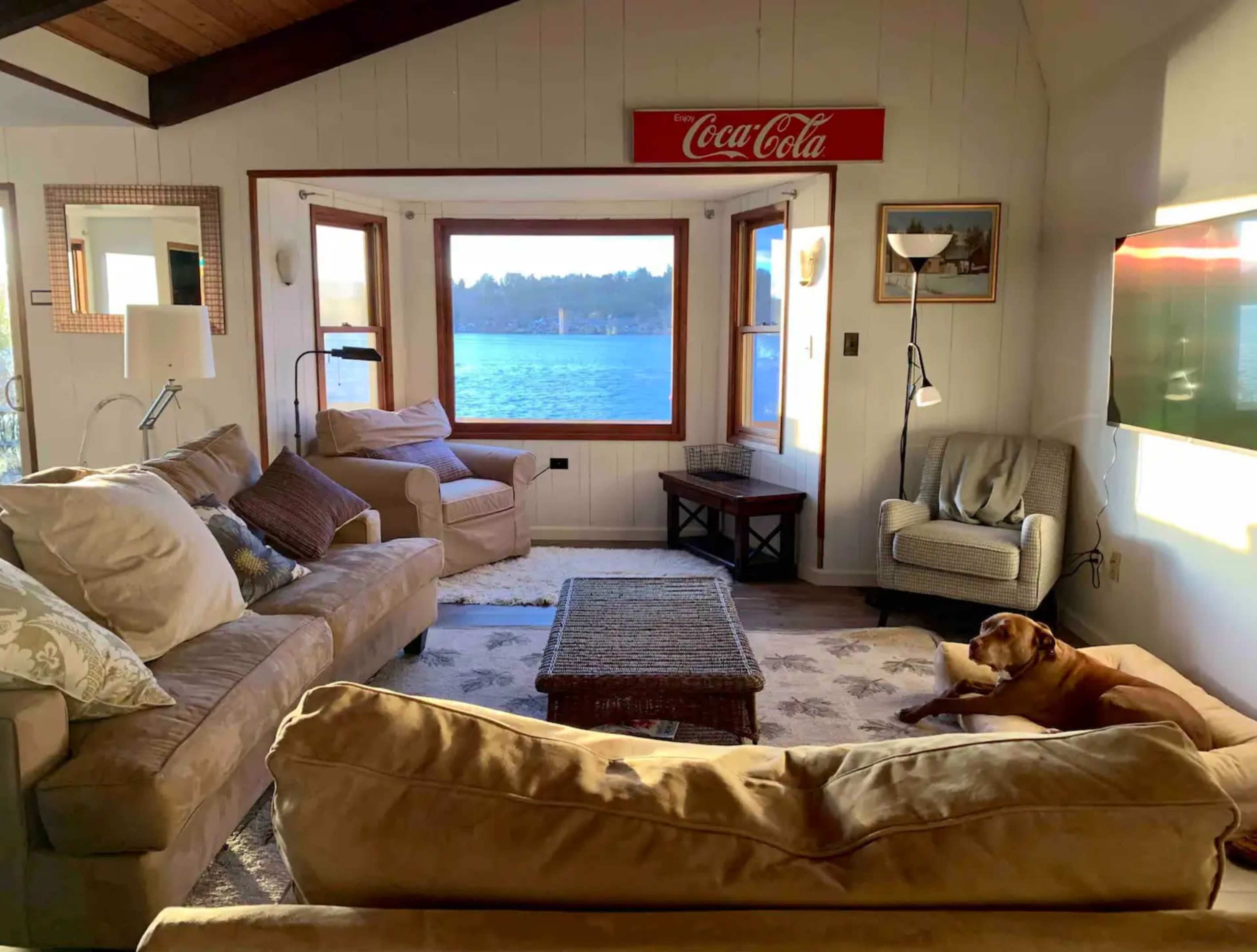 A cozy living room features two beige sofas, a coffee table, and a view of the water through large windows.