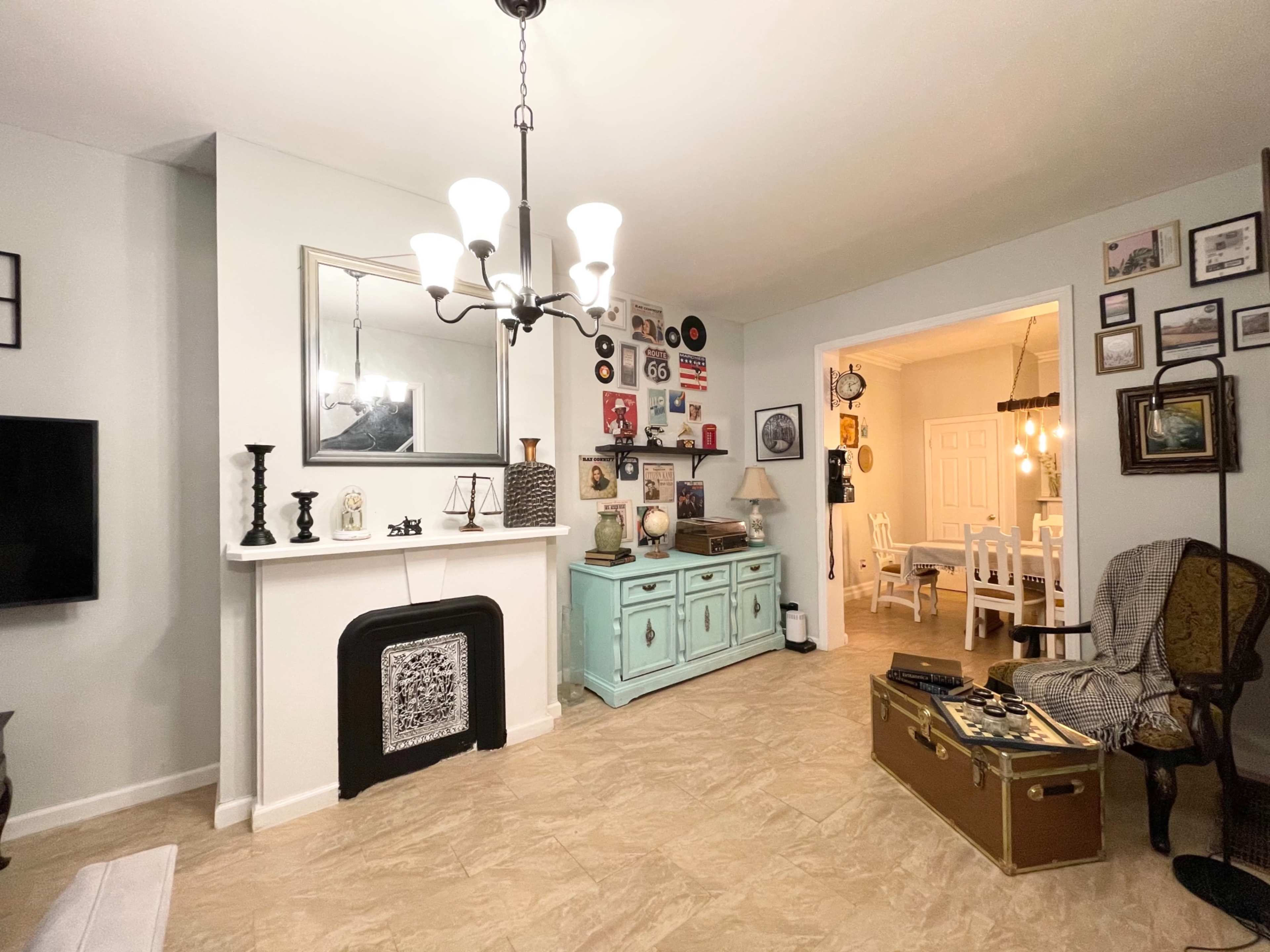 A living room with a fireplace, a turquoise sideboard, vintage decorations on the walls, and a dining area visible through an archway.