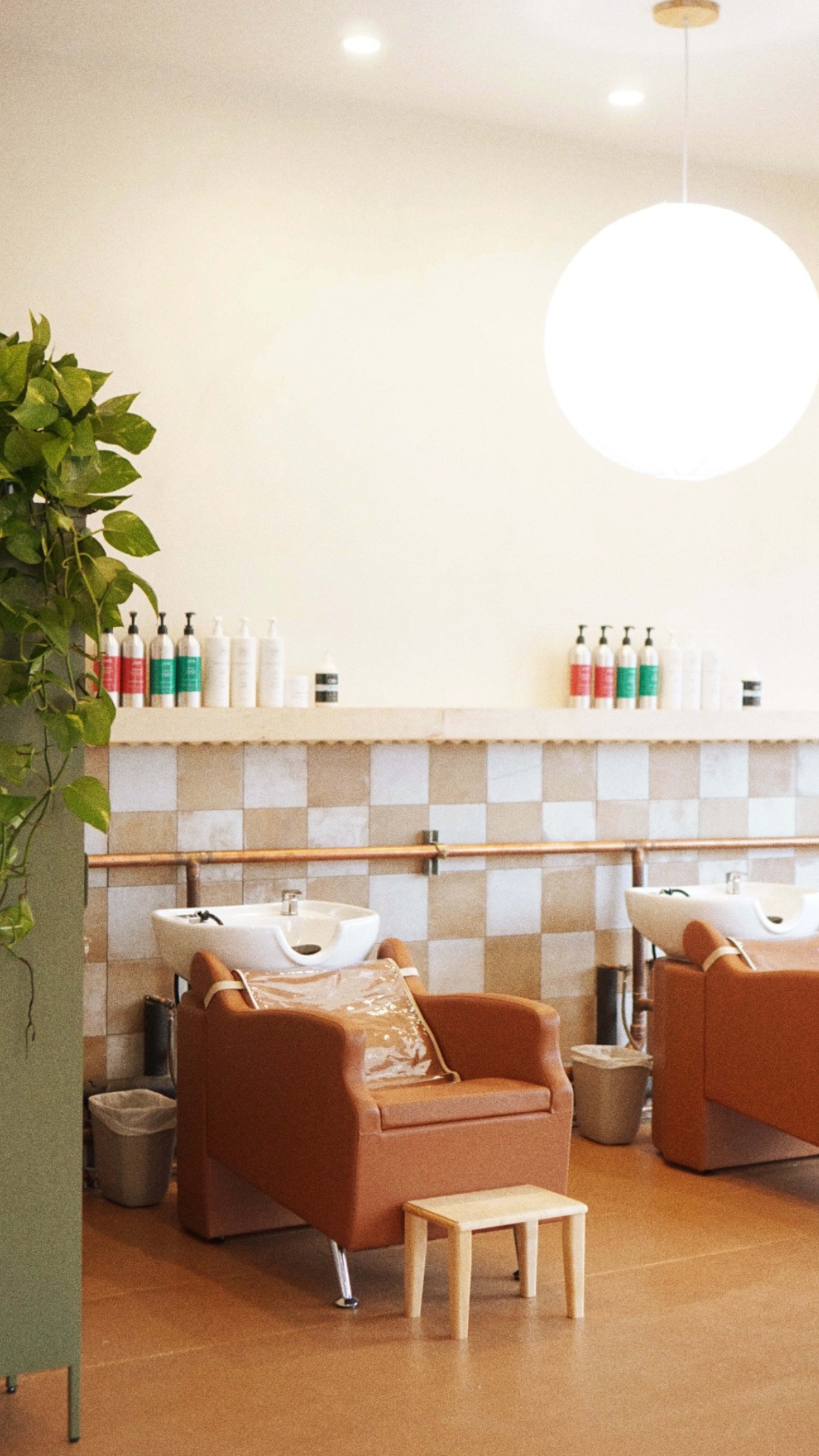 The image shows a modern hair salon with two washing stations, brown chairs, and a shelf of hair care products in the background.