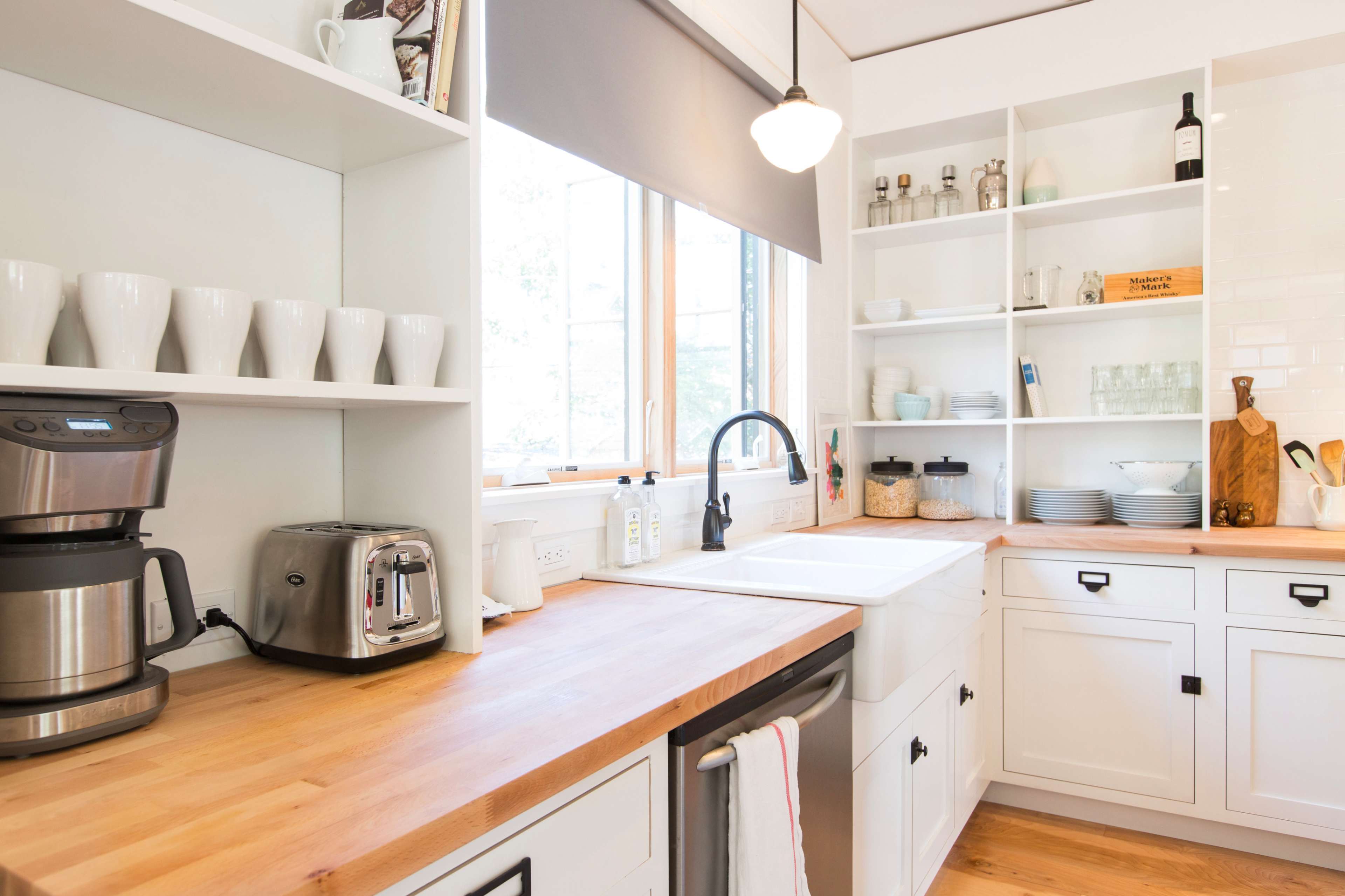 A modern kitchen with white cabinetry, a double sink, a coffee maker, and shelves filled with dishes and glassware.