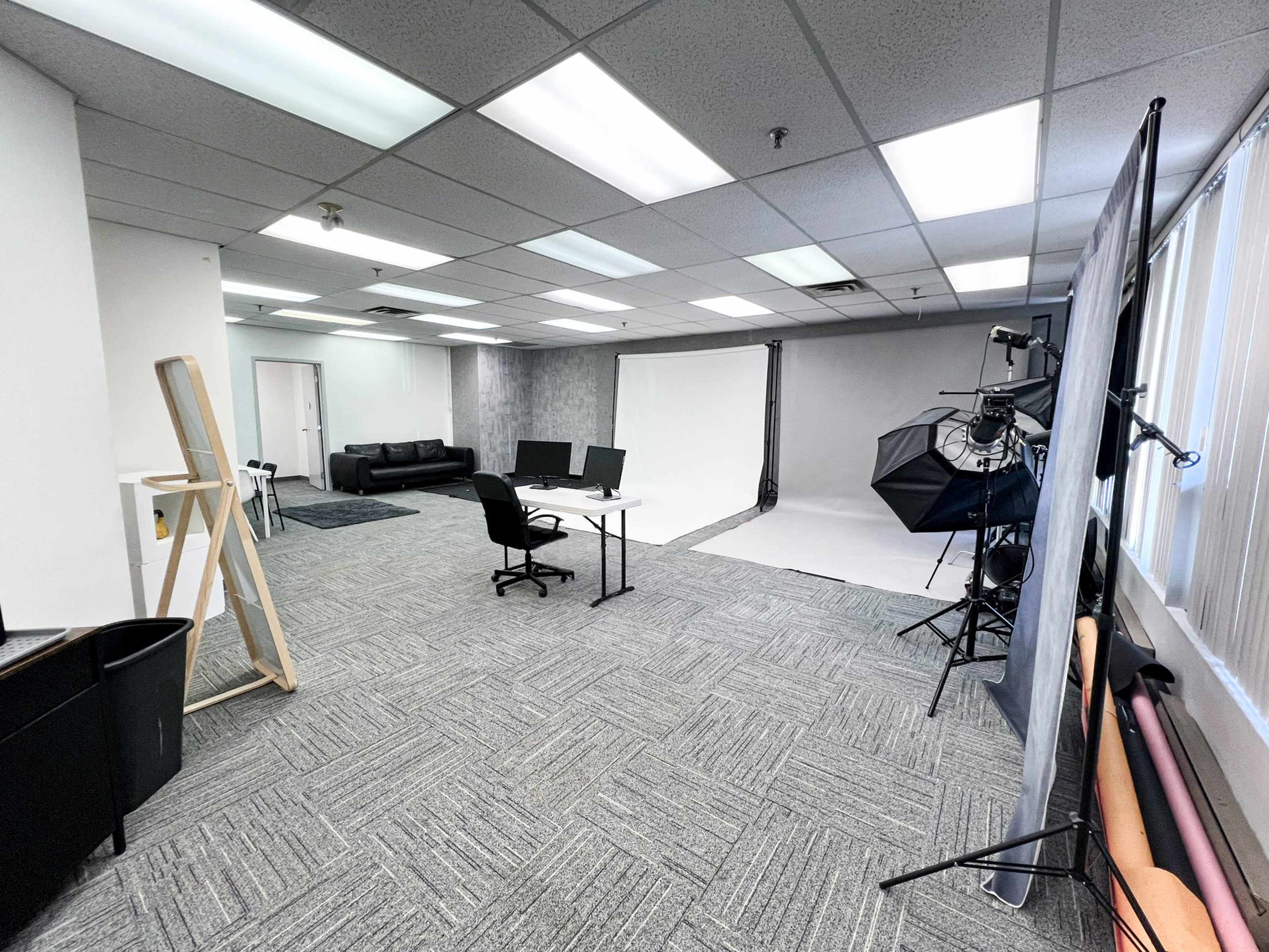 A photography studio with two workstations, a black couch, and equipment for photo shoots, including backdrops and lighting setups.