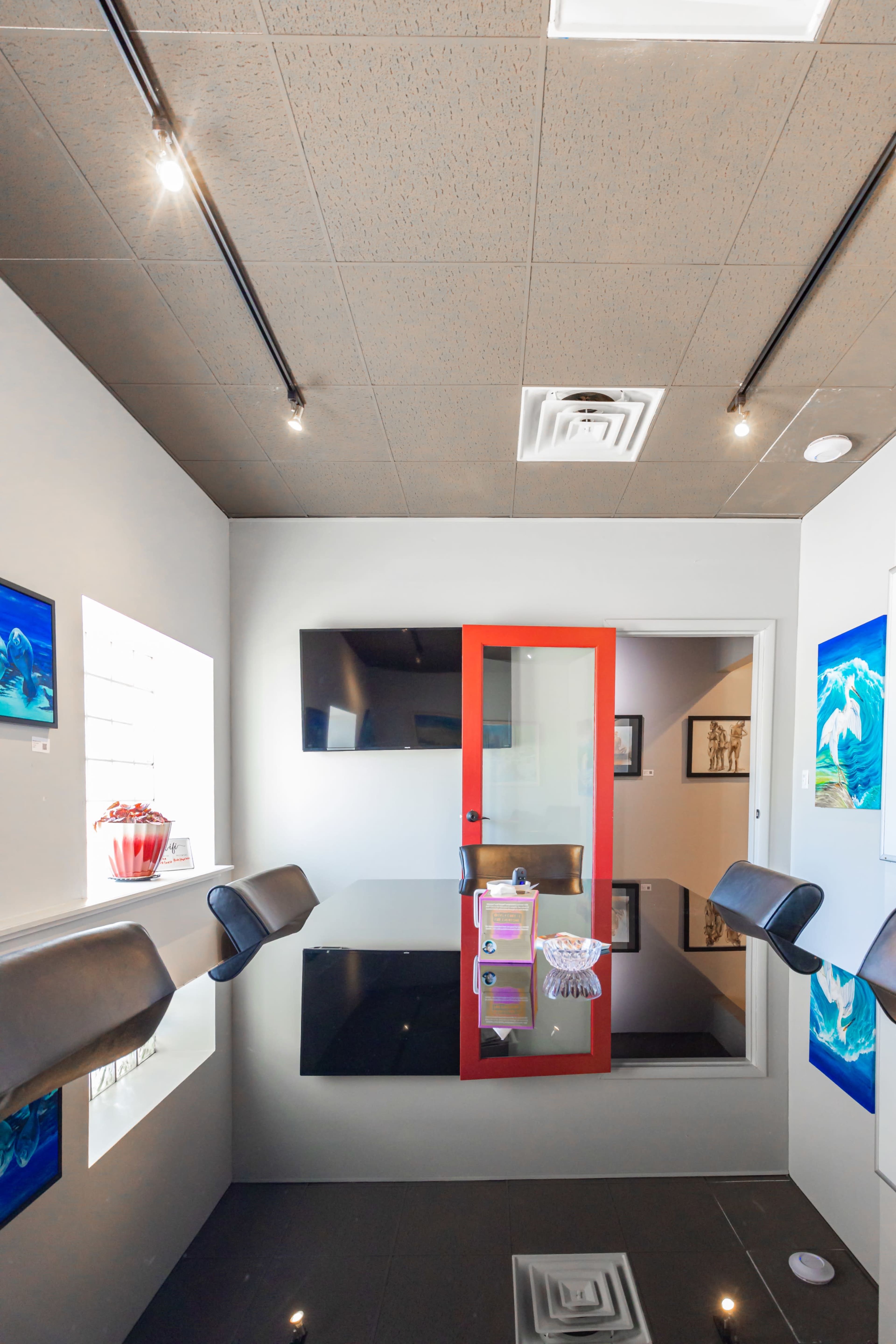 A modern conference room features a sleek black table, glass walls, and red accents, with artwork displayed on the walls.