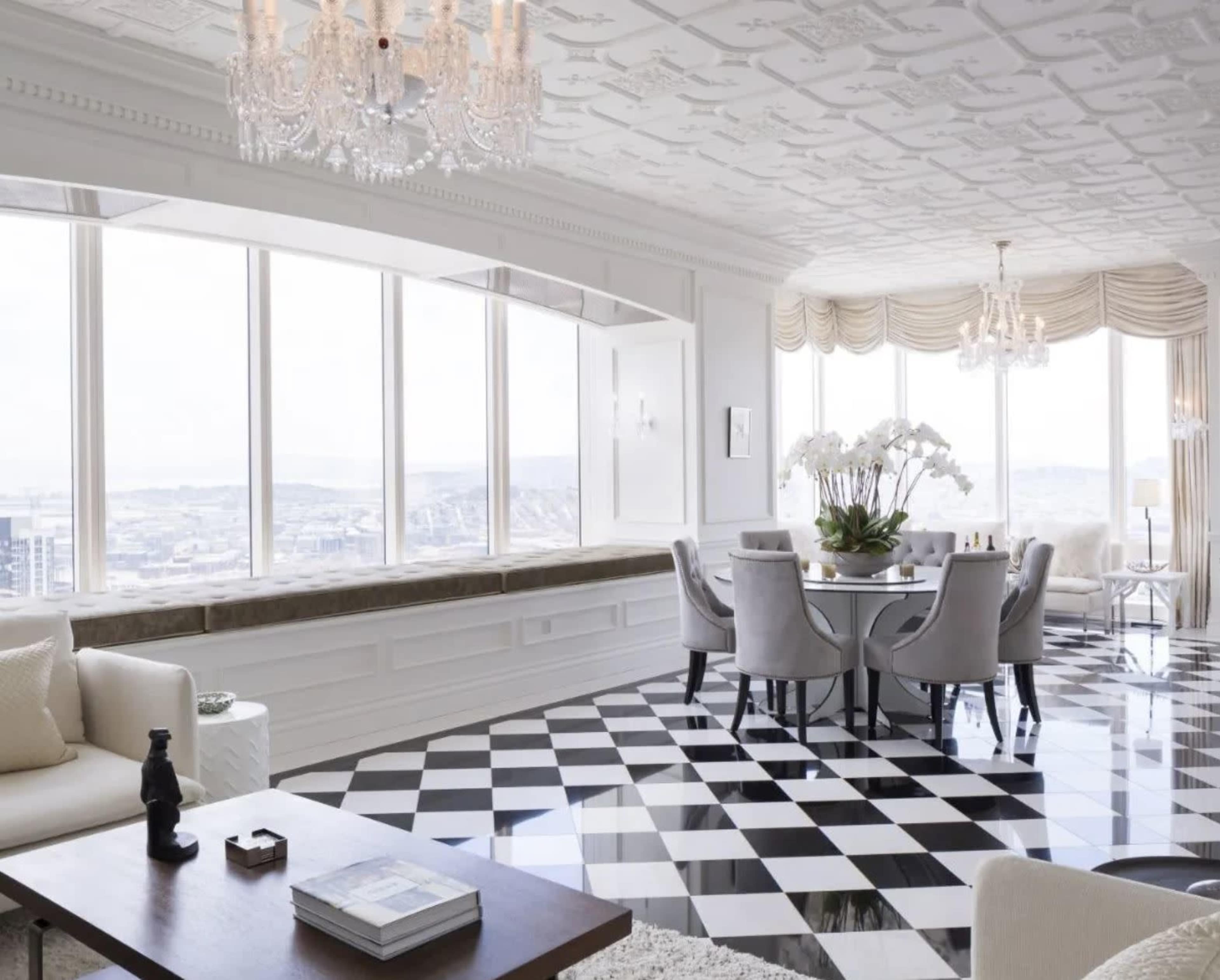A bright and modern dining room with a patterned black and white tiled floor, elegant furniture, and large windows offering a view of the city.