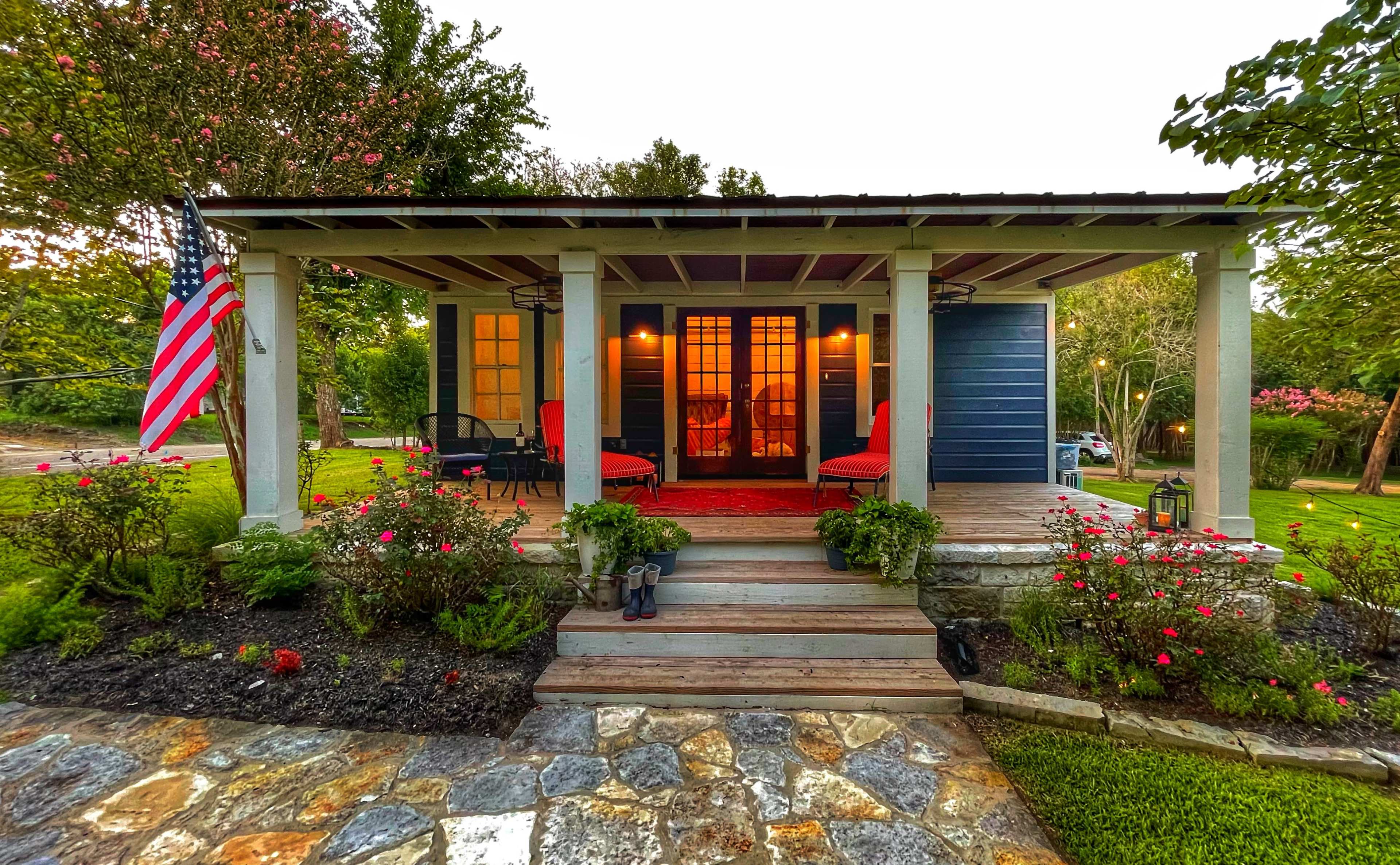 A charming front porch with red seating, surrounded by colorful flowers and a flag, welcomes visitors to a house.