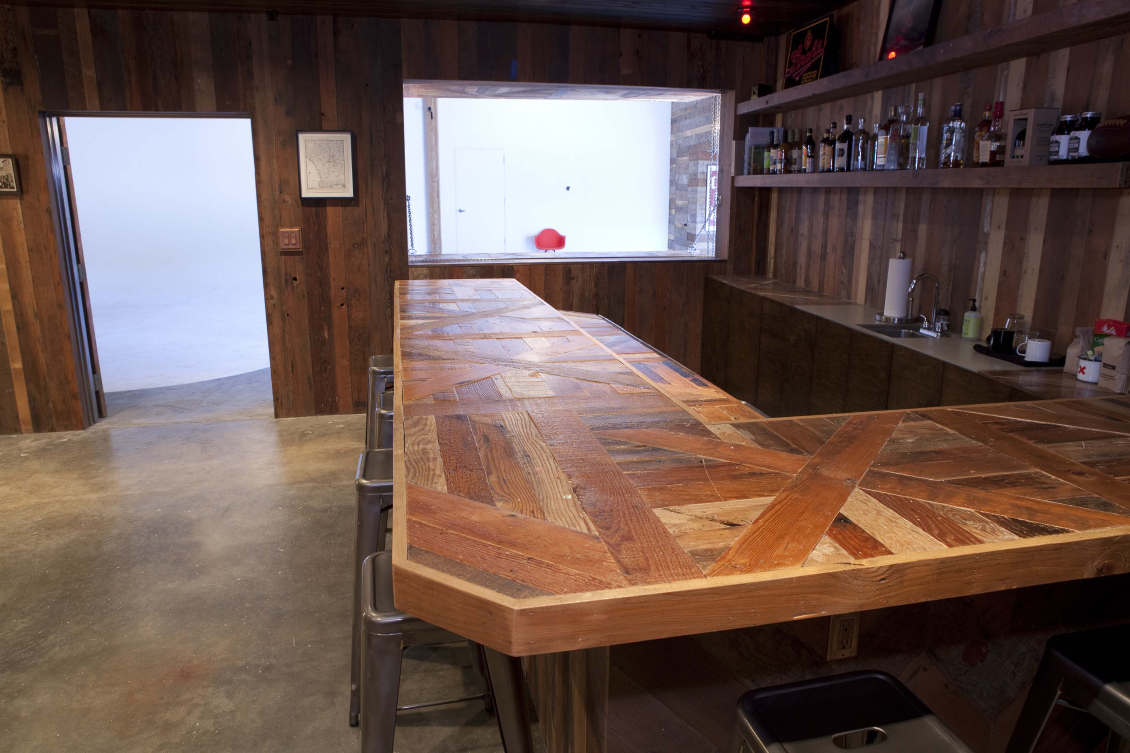 A wooden bar with a patterned countertop, surrounded by rustic wooden walls and a window that opens to a lighter space.