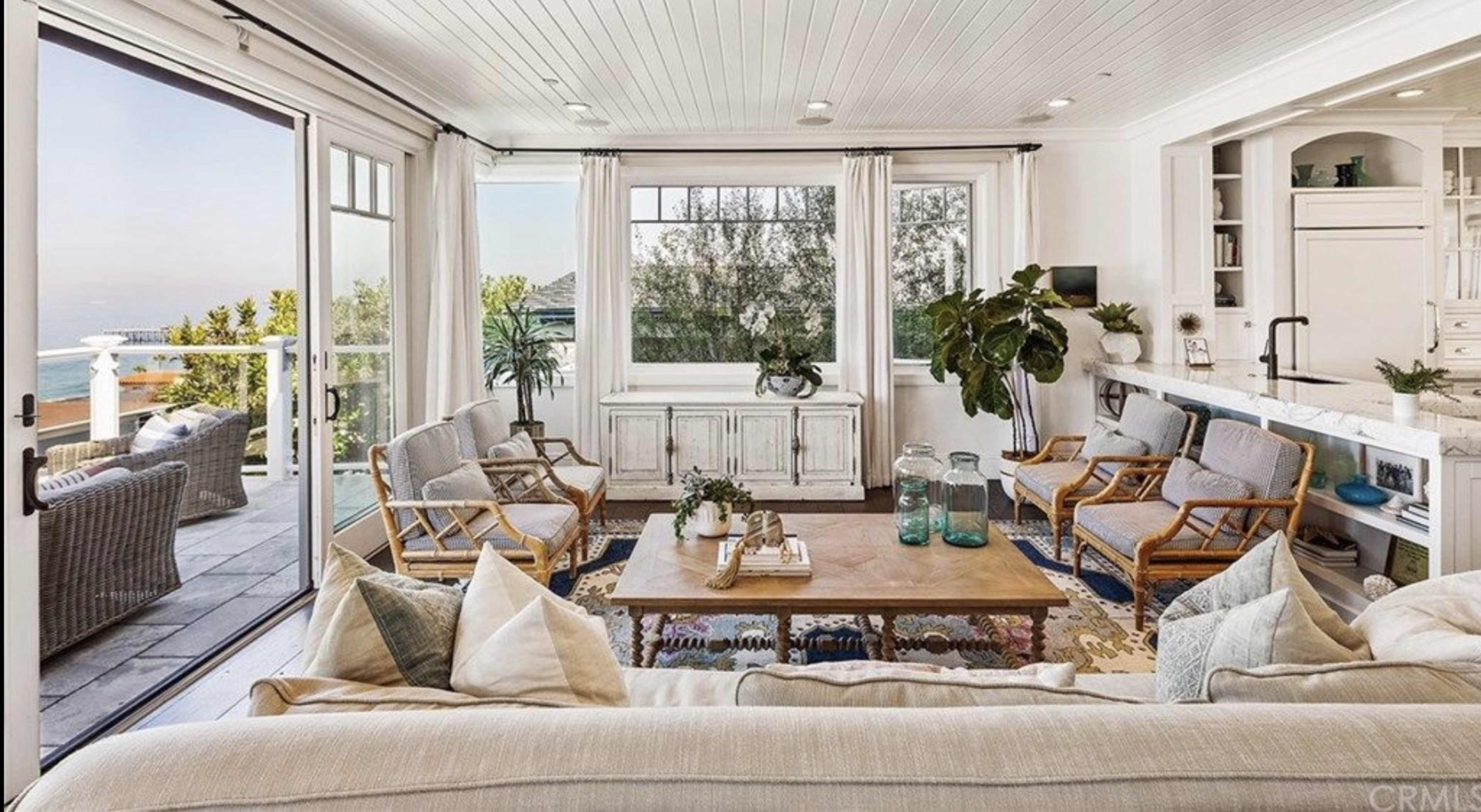 A bright living room features a large window with a view, a wooden coffee table at the center, and comfortable seating arranged around it.