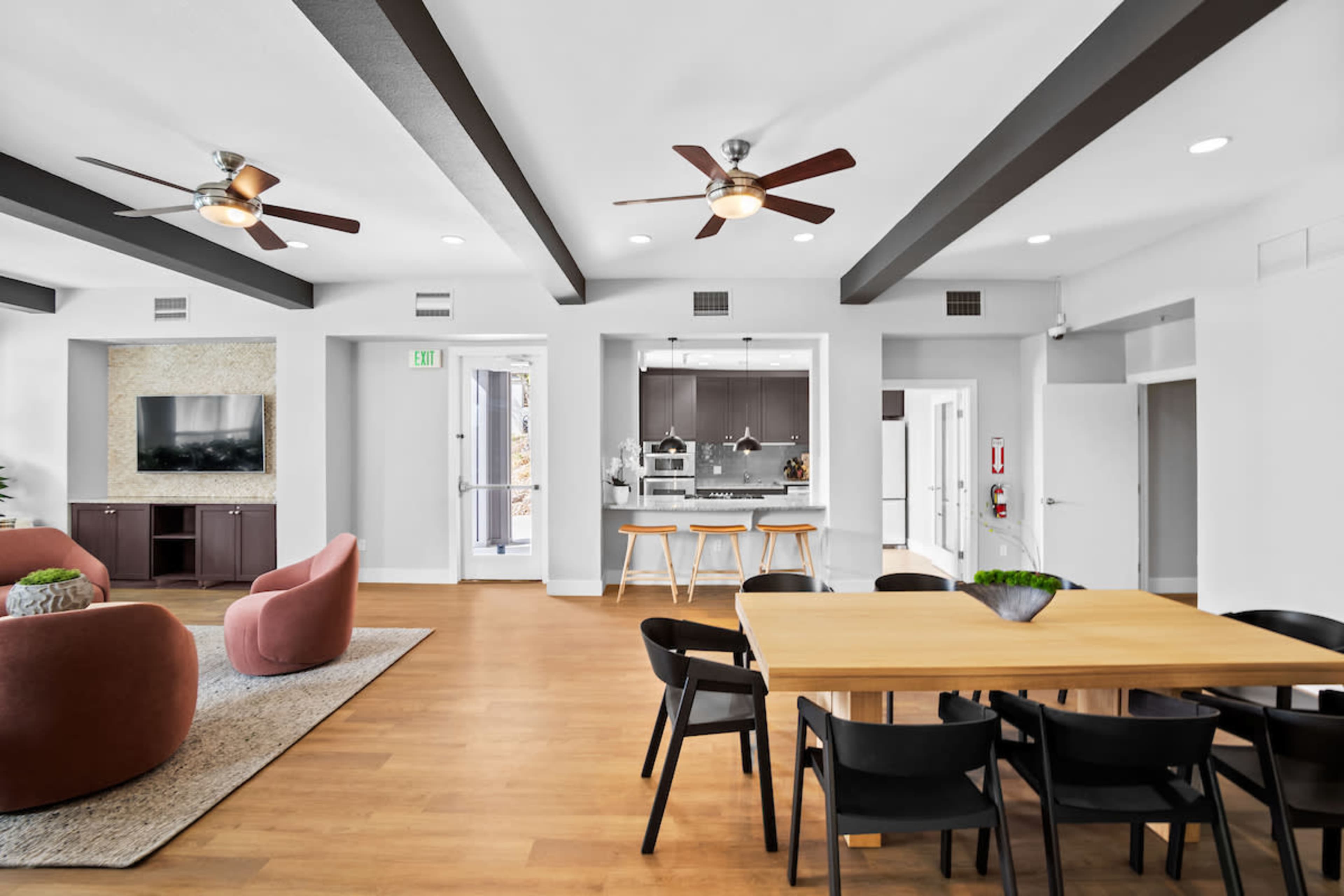 The image shows a modern open-concept living area featuring a dining table, seating area with two large chairs, and a kitchen in the background.