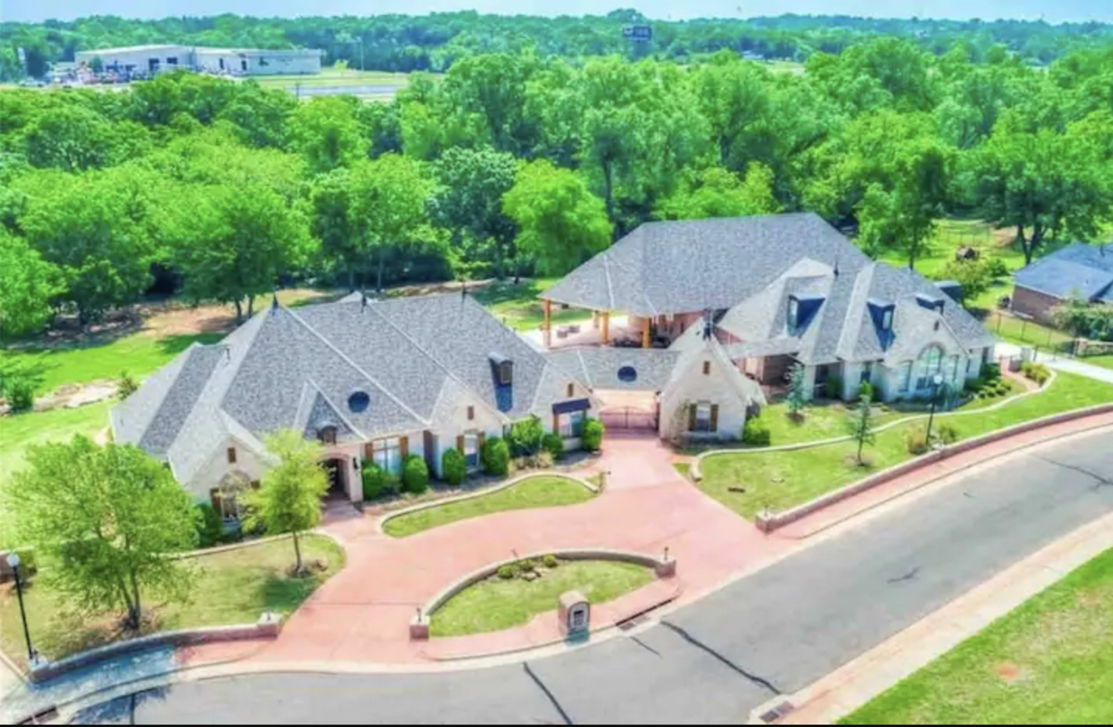 A large residential property featuring two distinct buildings, surrounded by greenery and landscaped gardens, situated on a curved street.