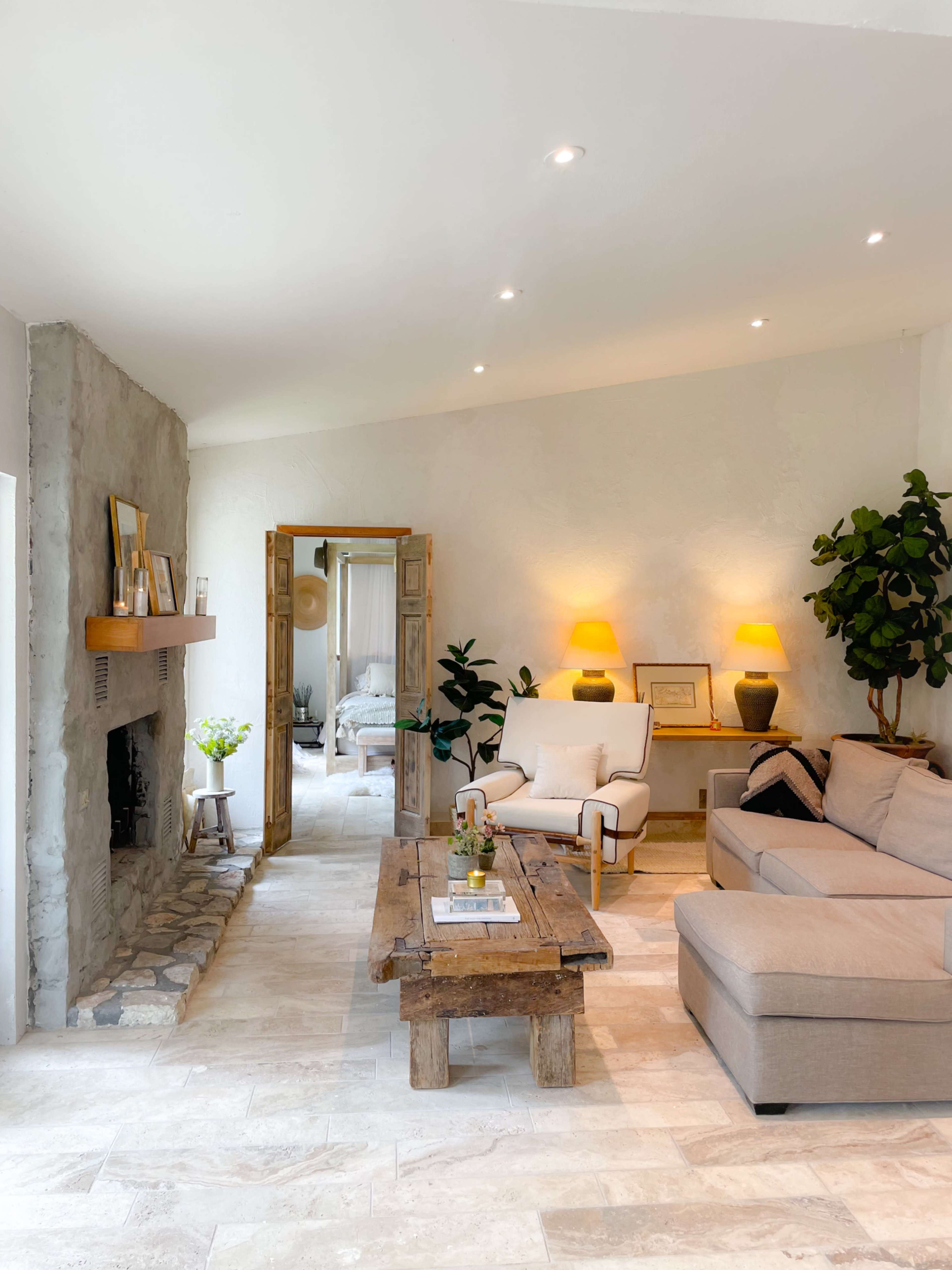A modern living room featuring a stone fireplace, a wooden coffee table, a gray sectional sofa, and plants, with warm lighting accentuating the space.