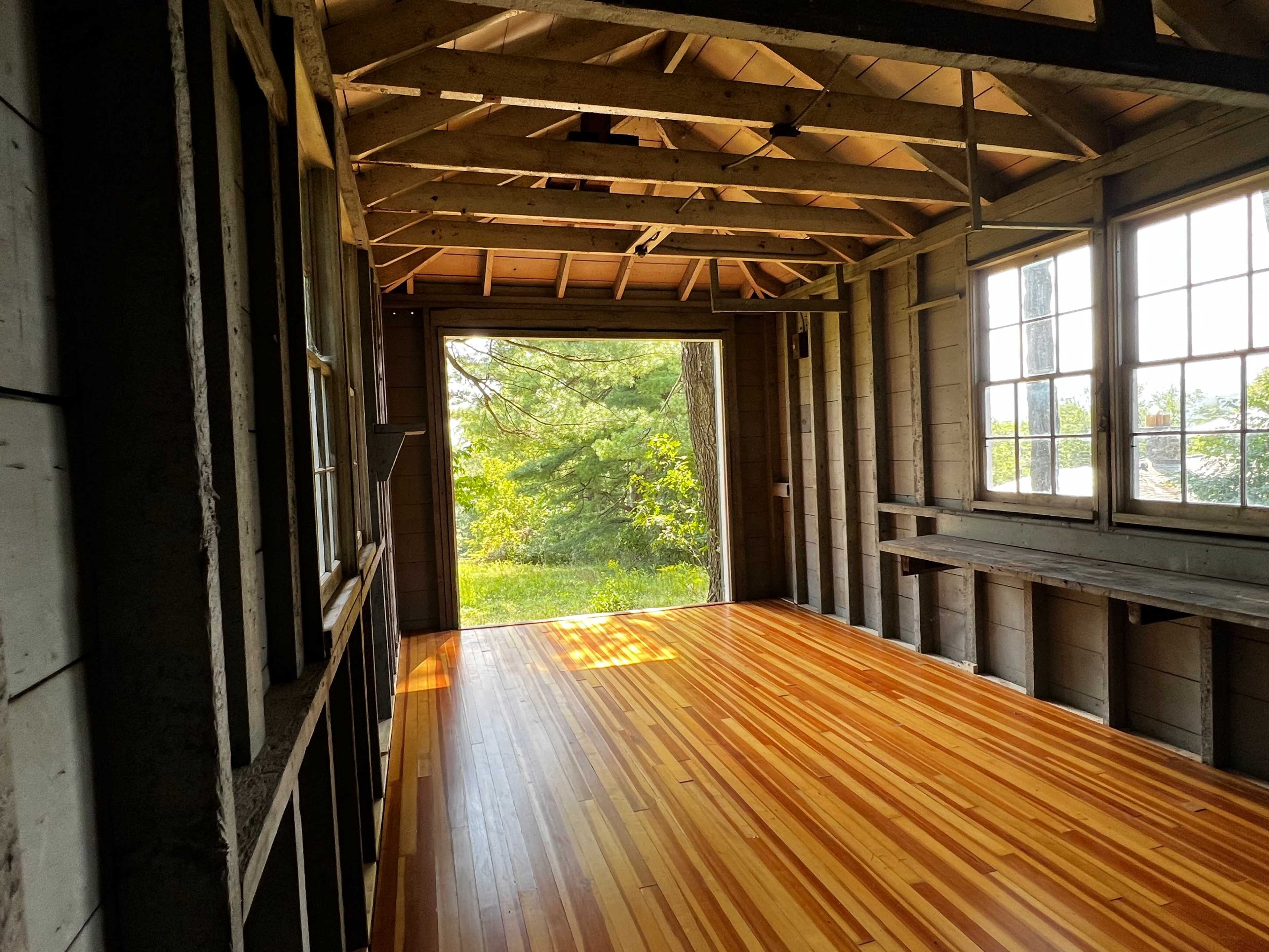 The interior of an unfinished wooden room with large windows overlooking a green landscape.