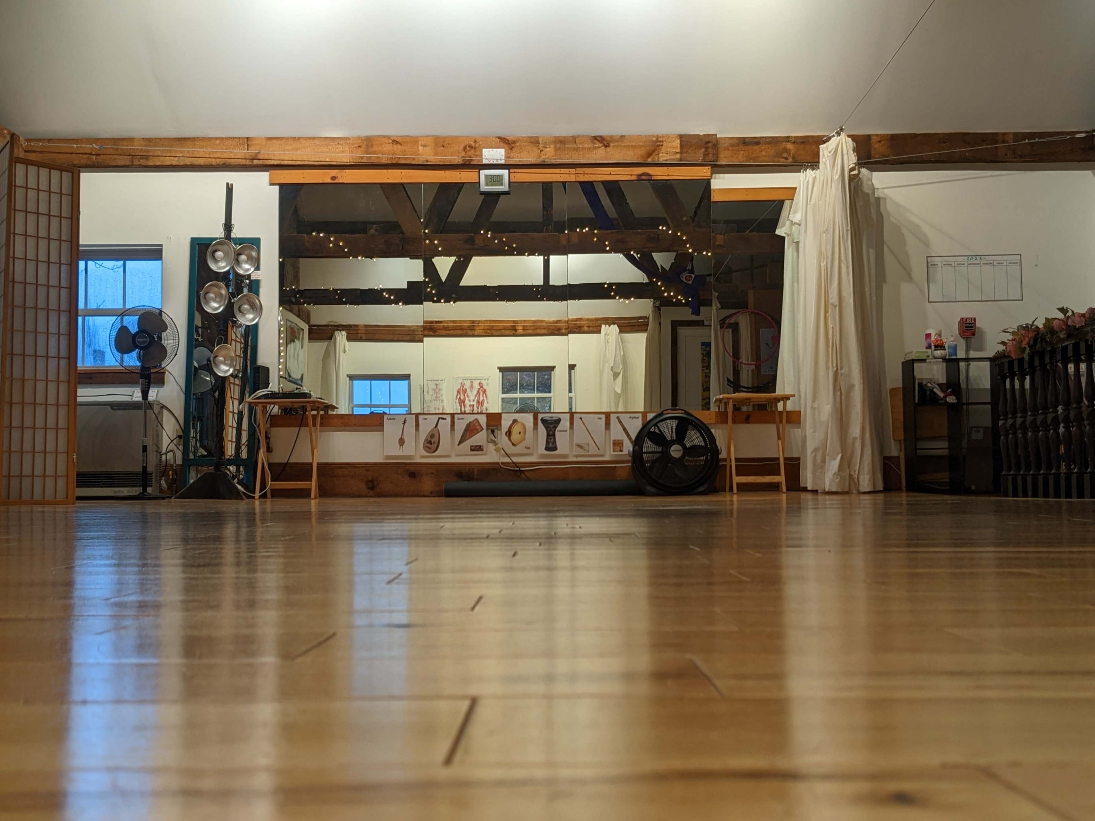 A spacious, minimally decorated interior with wooden floors, a large mirror reflecting several art pieces, and light filtering through windows.