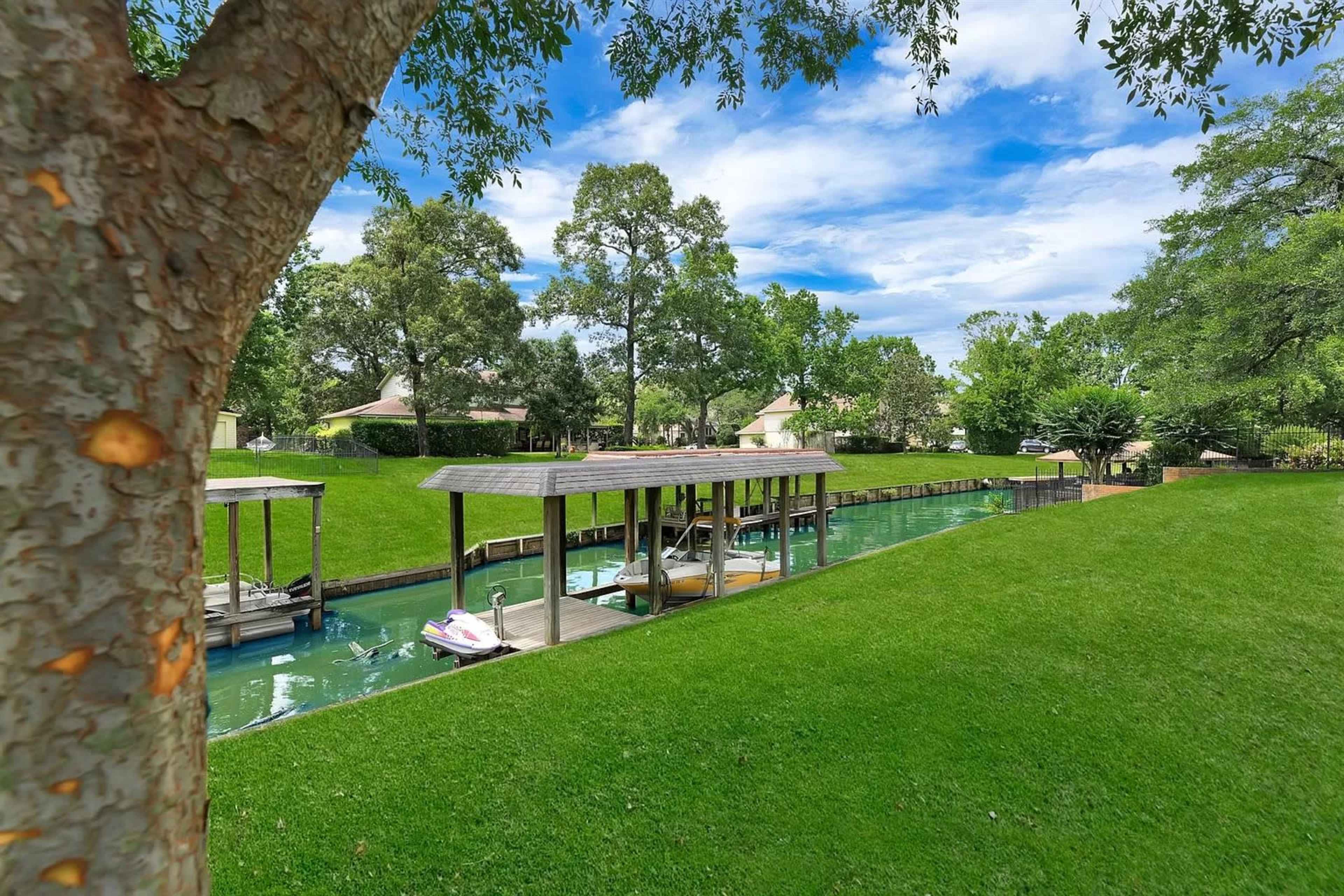 A fishable canal lined with a manicured green lawn and covered boat docks on one side.