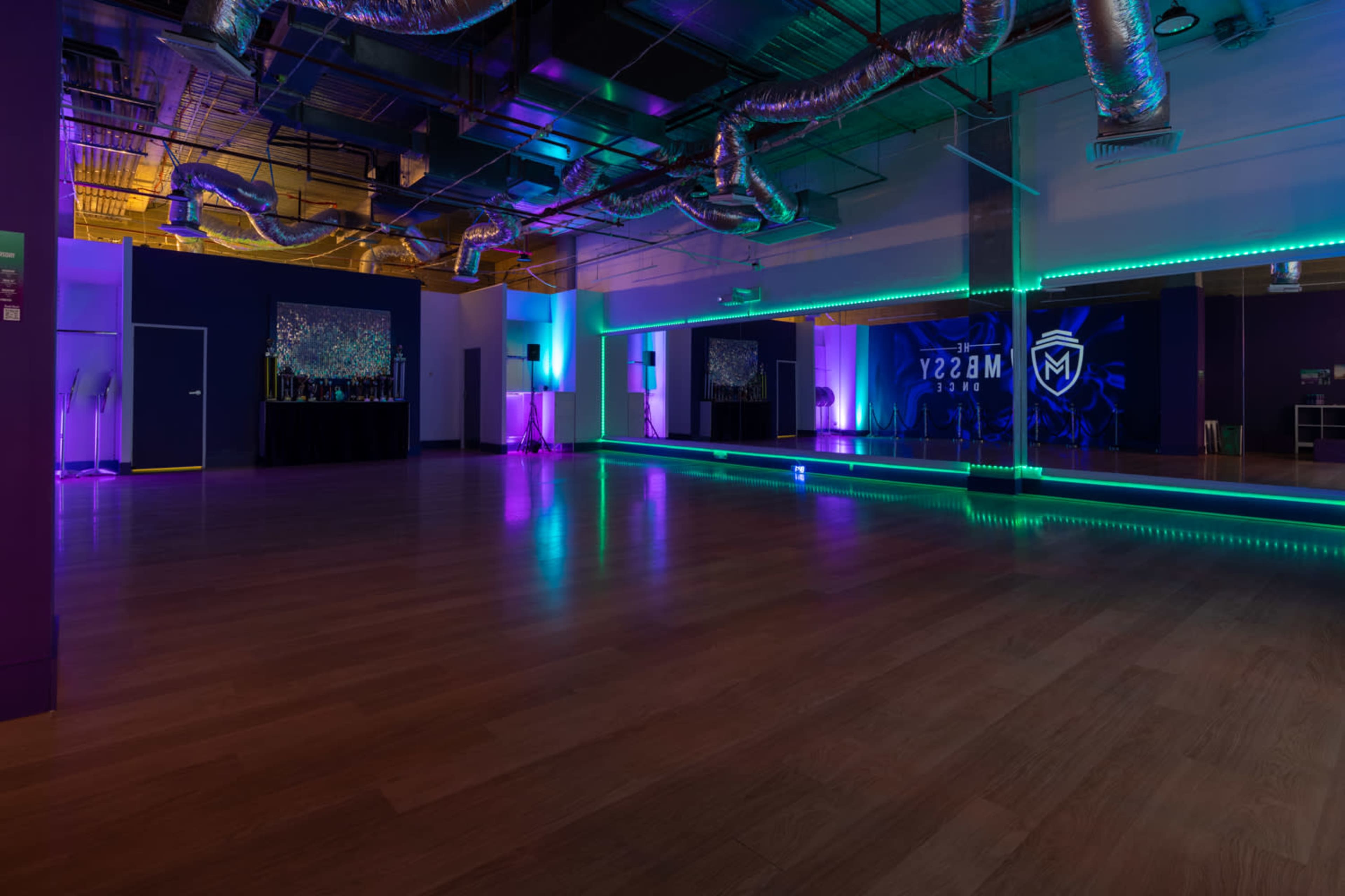 The image shows an empty dance studio with colorful lighting, reflective walls, and a large mirror.