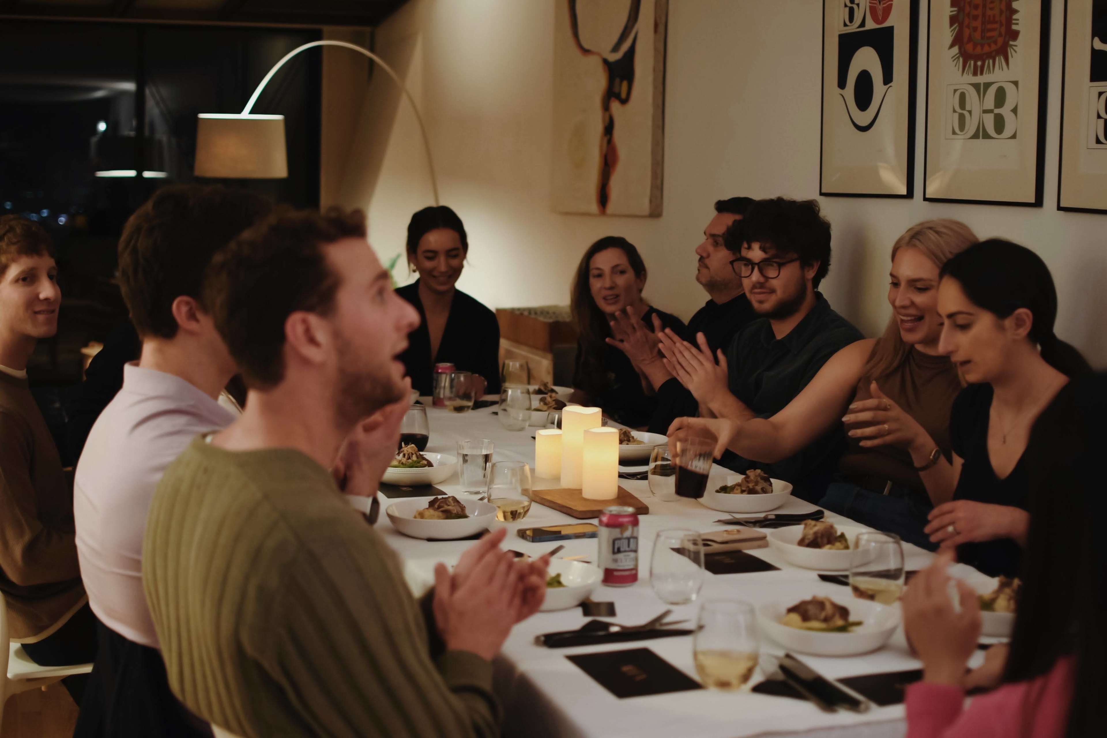 A group of people is seated around a dinner table, enjoying a meal and participating in lively conversation.