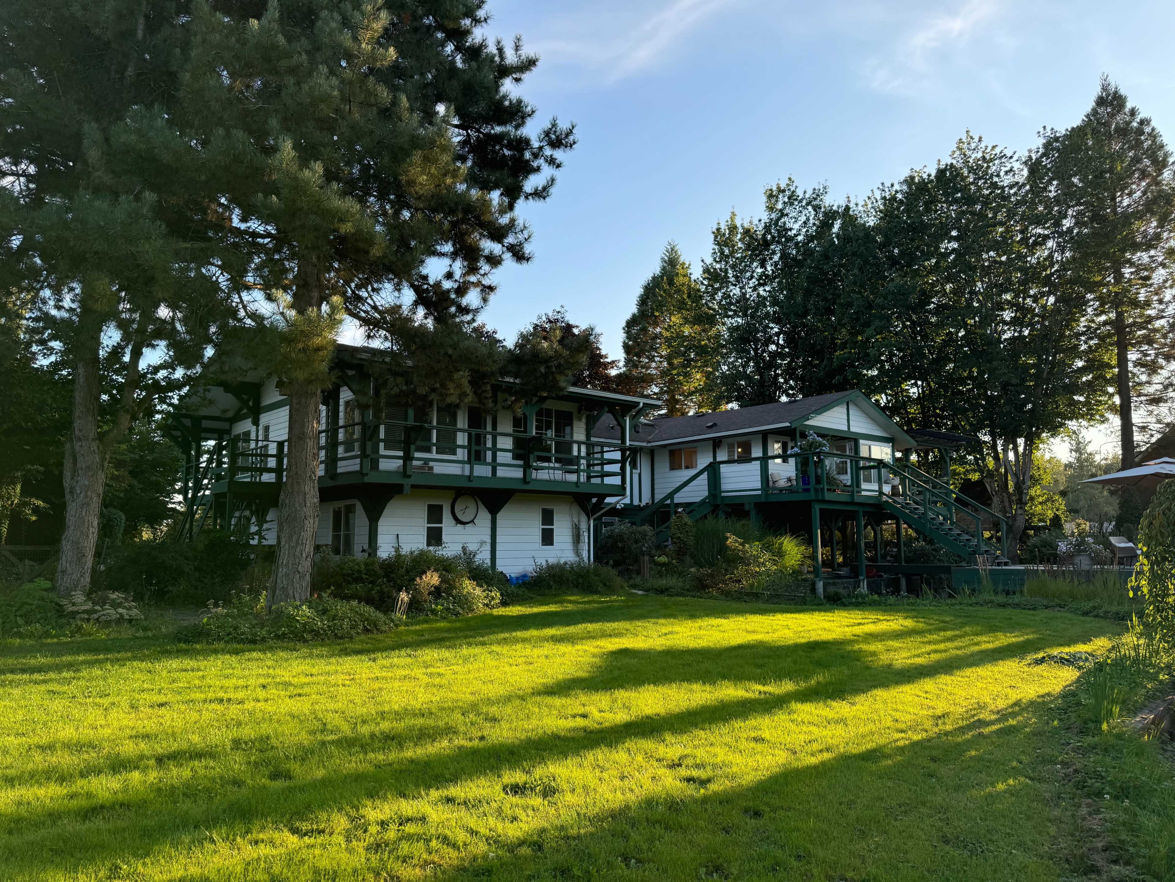 The image shows a two-story white house with green accents surrounded by trees and a well-maintained grassy yard.
