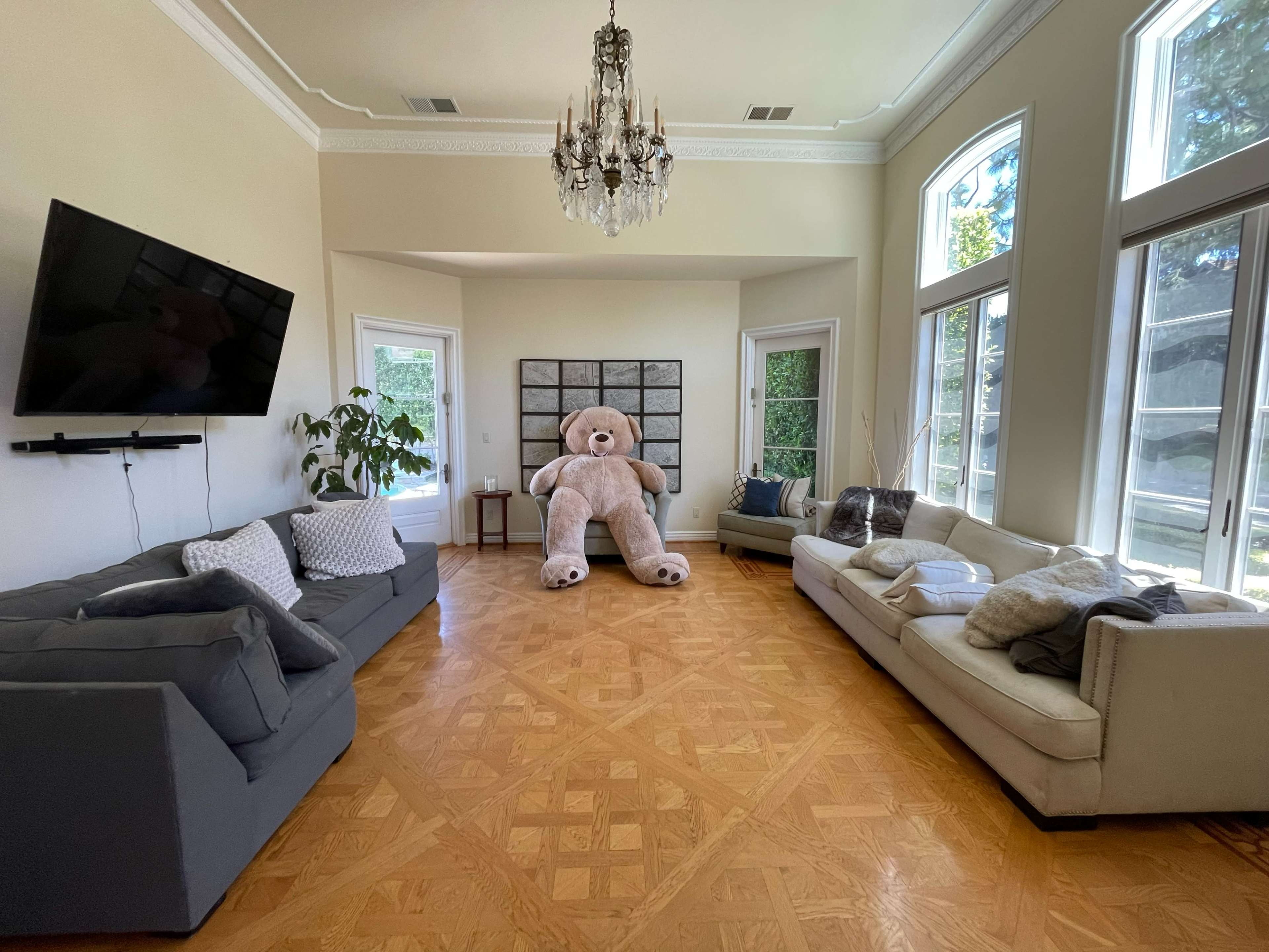 A spacious living room features two couches, a large teddy bear, and a television mounted on the wall.