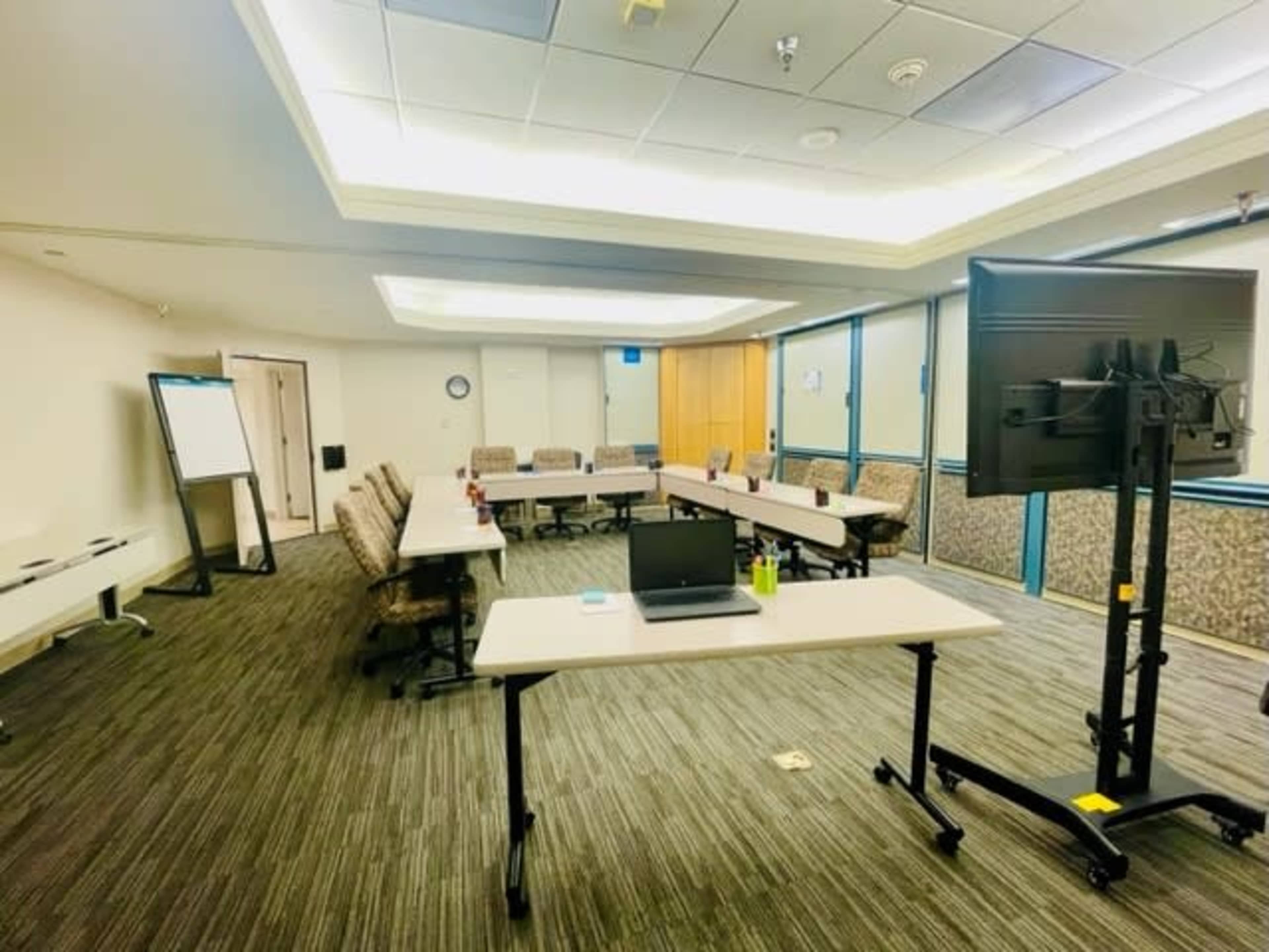 A conference room is set up with several tables, chairs, a laptop, and a large screen for presentations.