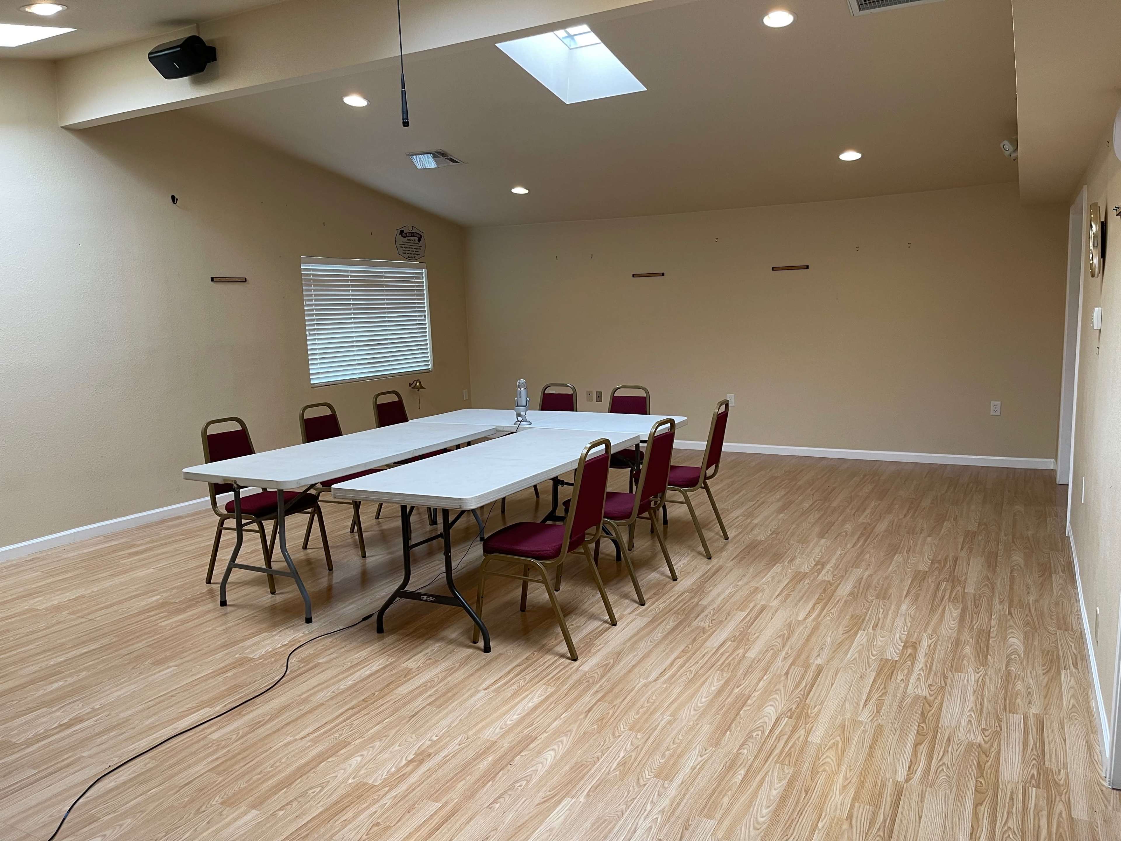 A brightly lit meeting room features a long rectangular table surrounded by chairs and a skylight above.