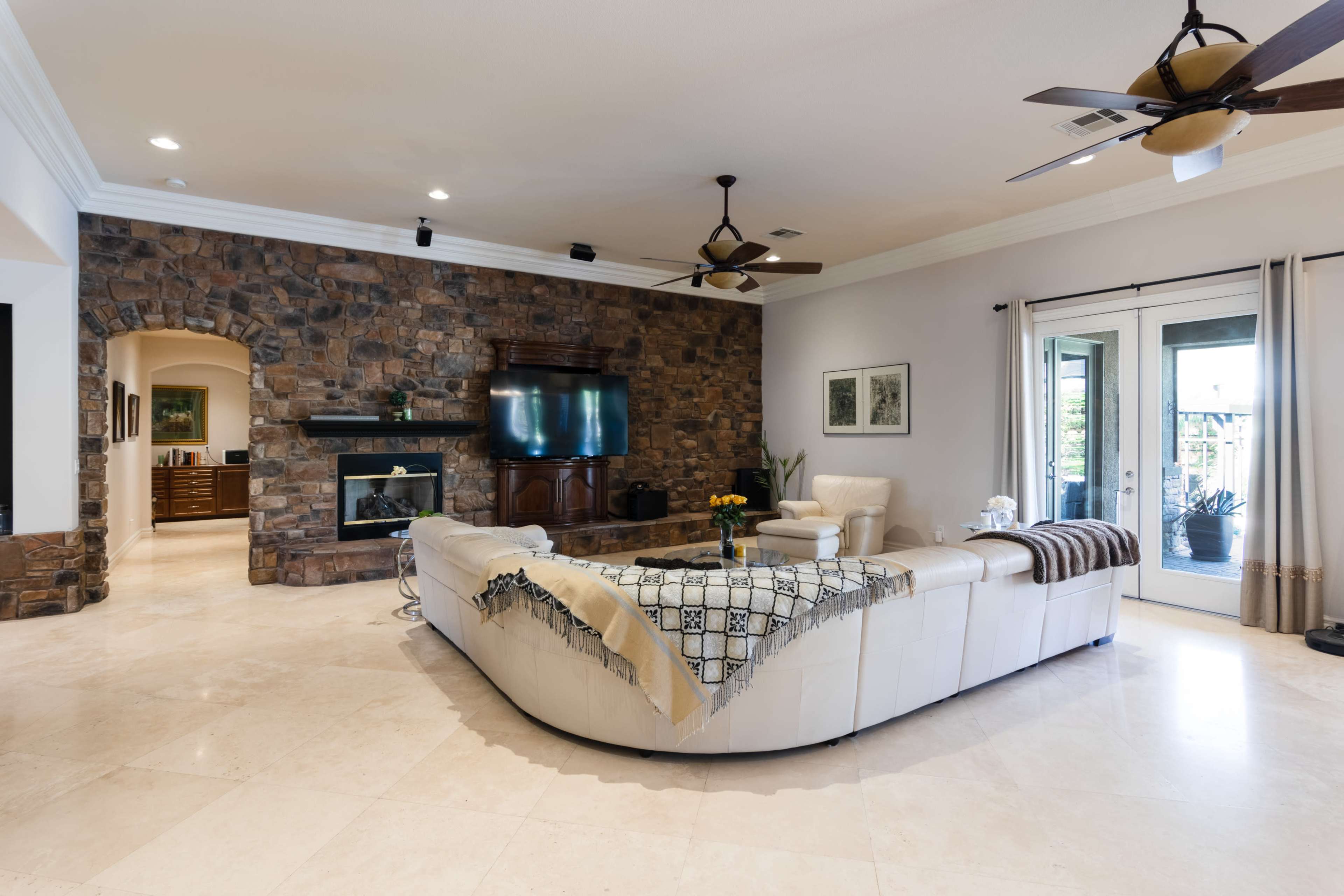 The living room features a large curved sofa, a stone accent wall, and sliding glass doors leading to an outdoor area.