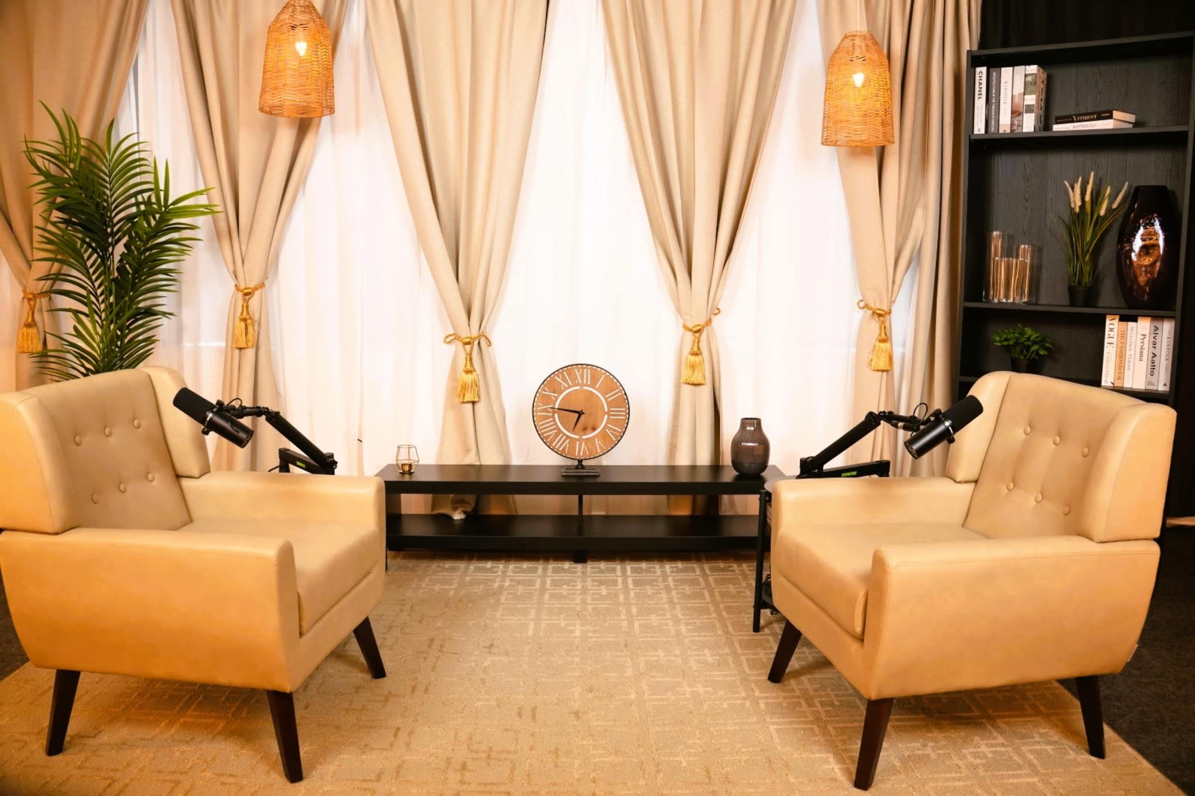 The image shows a cozy seating area with two beige armchairs facing a minimalist coffee table, surrounded by elegant curtains and decorative items.