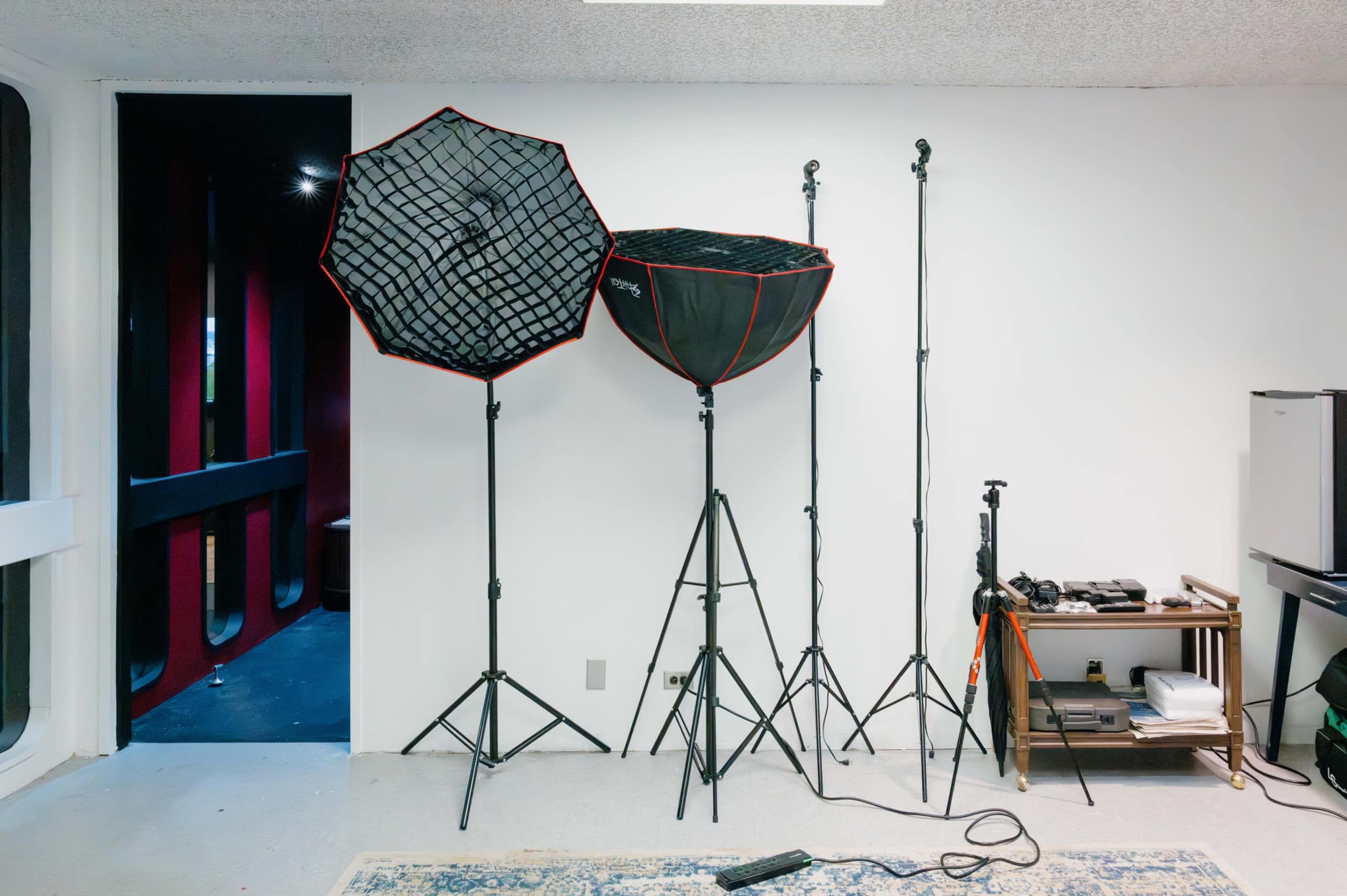 The image shows three softbox light setups on stands positioned against a plain wall in a room.