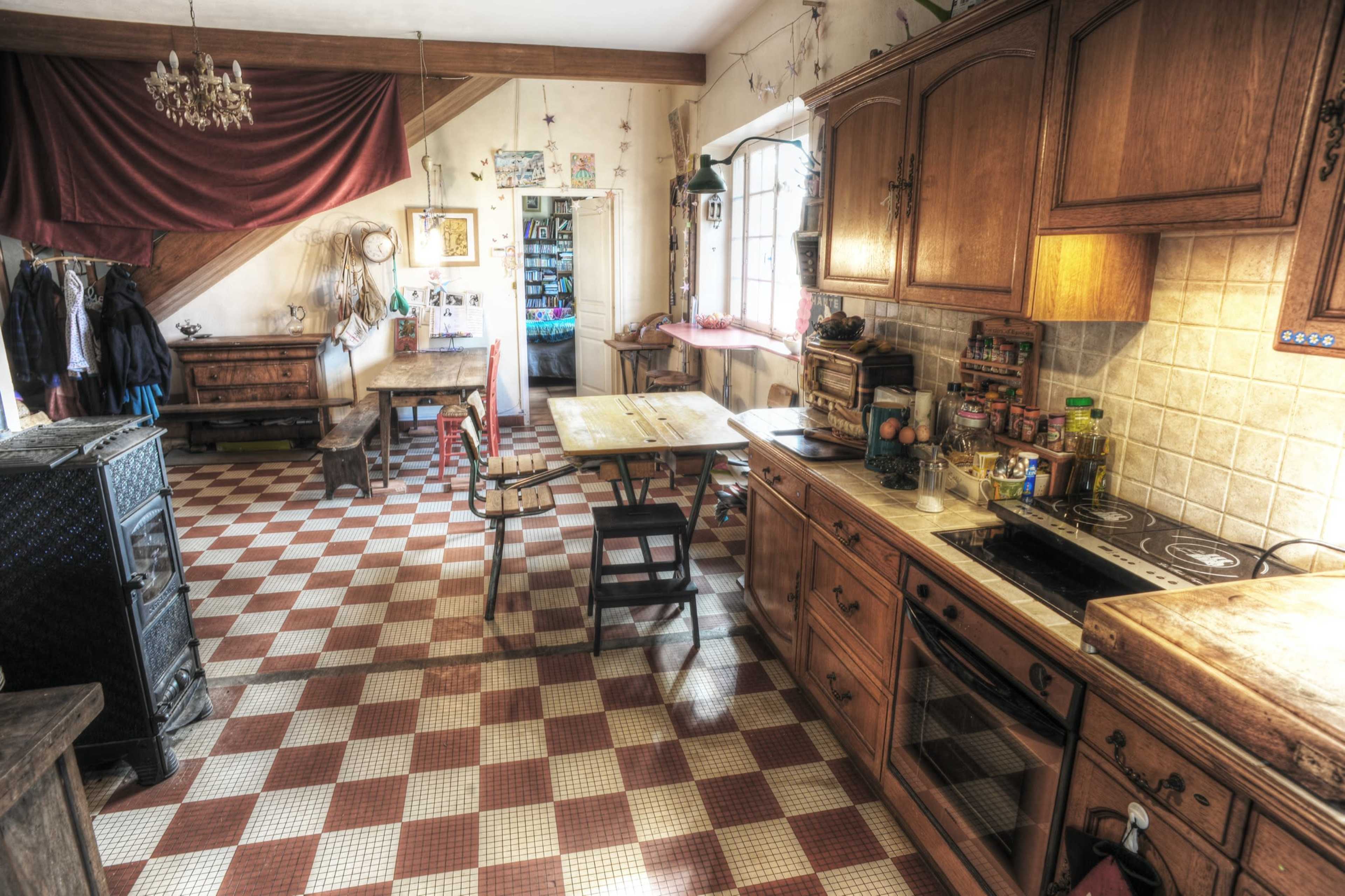 The image shows a vintage kitchen with checkered flooring, wooden cabinets, a table, and various kitchen utensils arranged on the counters.