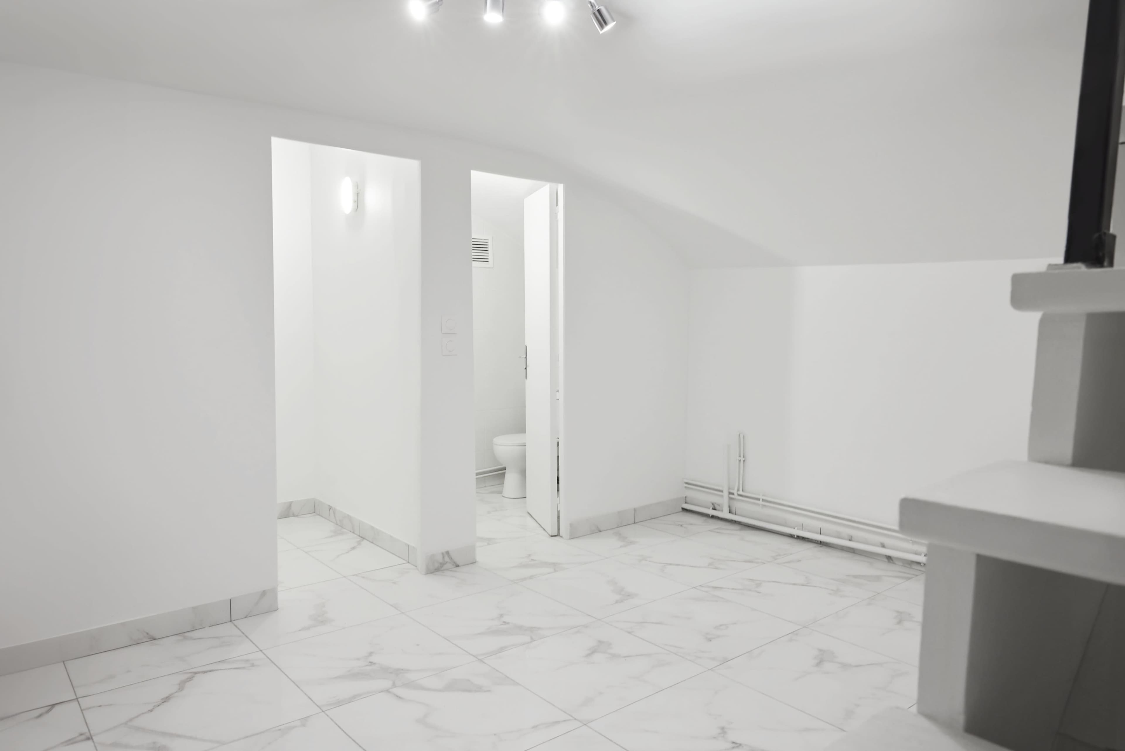 The image shows a sparsely furnished, white room with marble tile flooring and a door leading to a bathroom.
