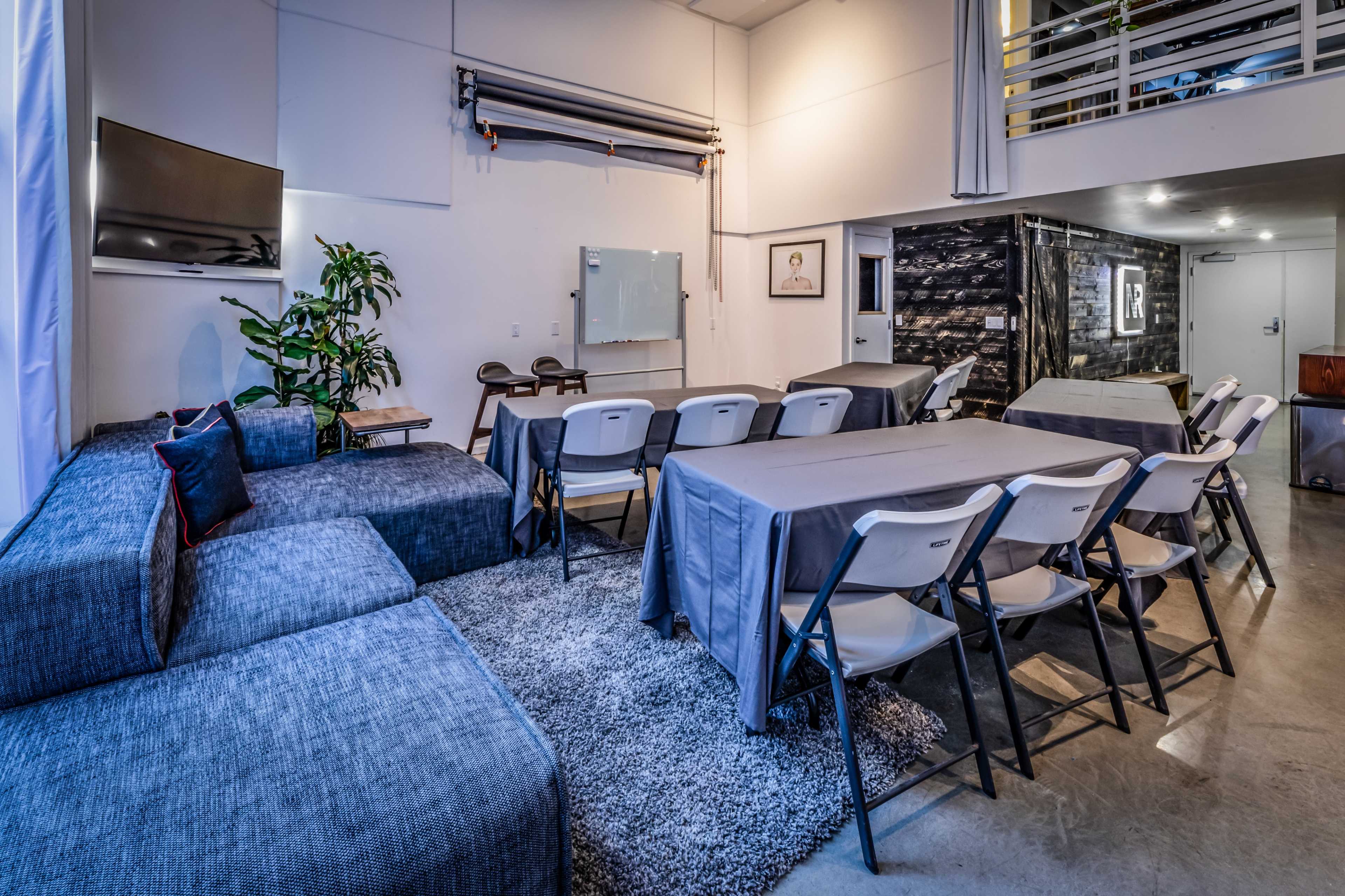 A modern meeting space featuring a sectional sofa, folding tables, and a whiteboard, with a sleek design and neutral color scheme.