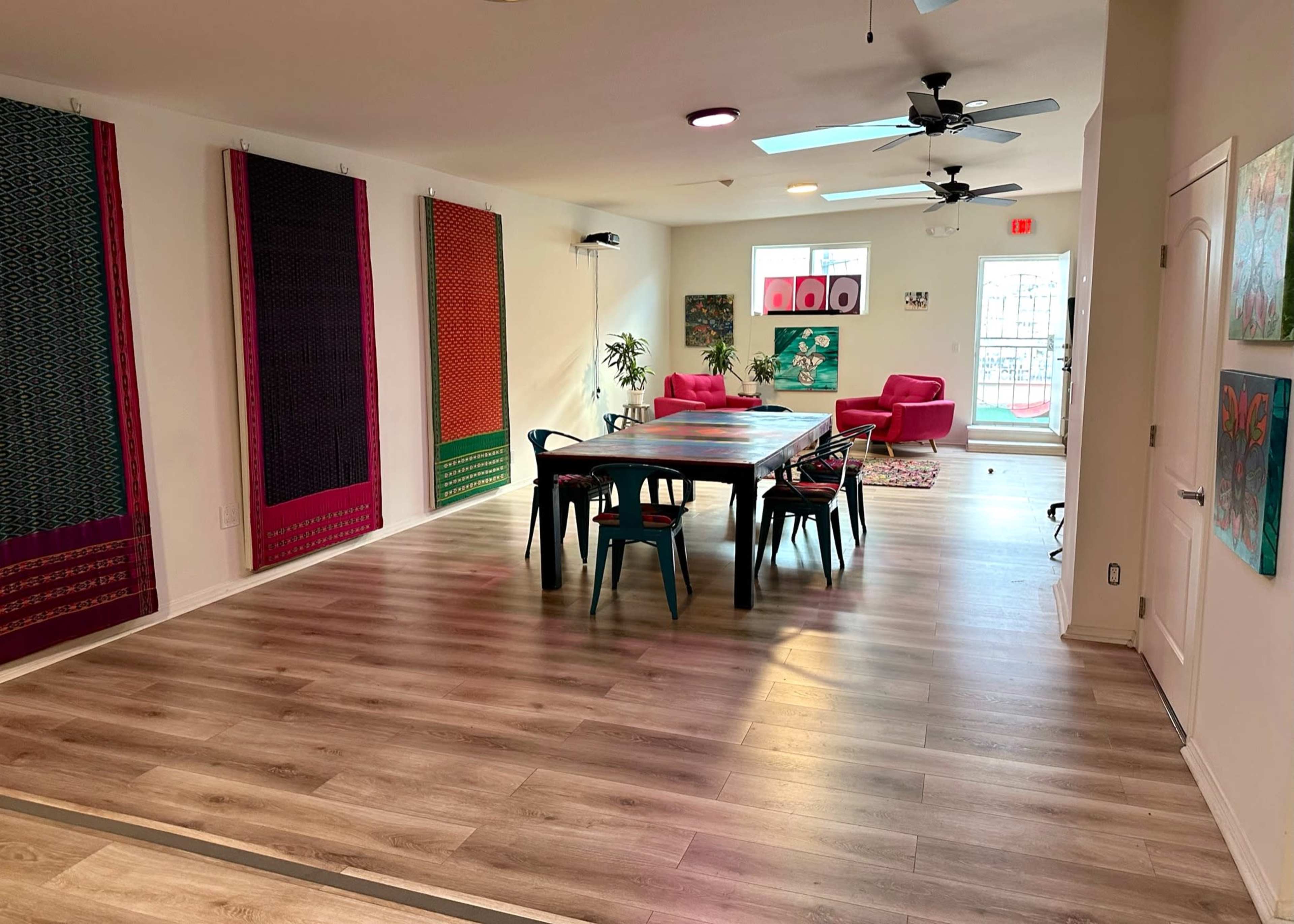 A spacious, modern room with a large table surrounded by chairs, colorful wall hangings, and a seating area with red chairs.