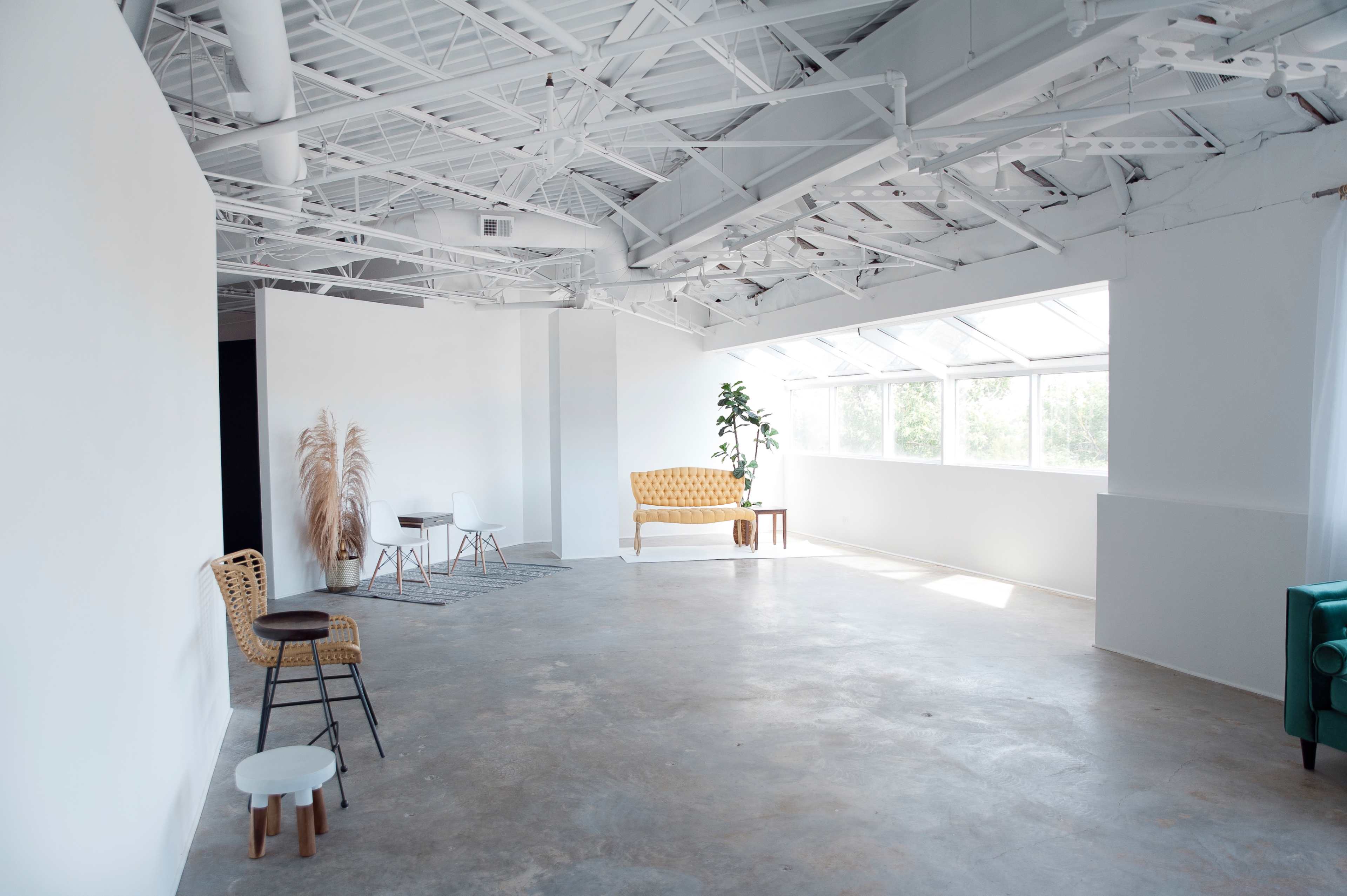 A bright, open studio space with white walls, large windows, and minimalist furniture, including a yellow couch and a textured rug.