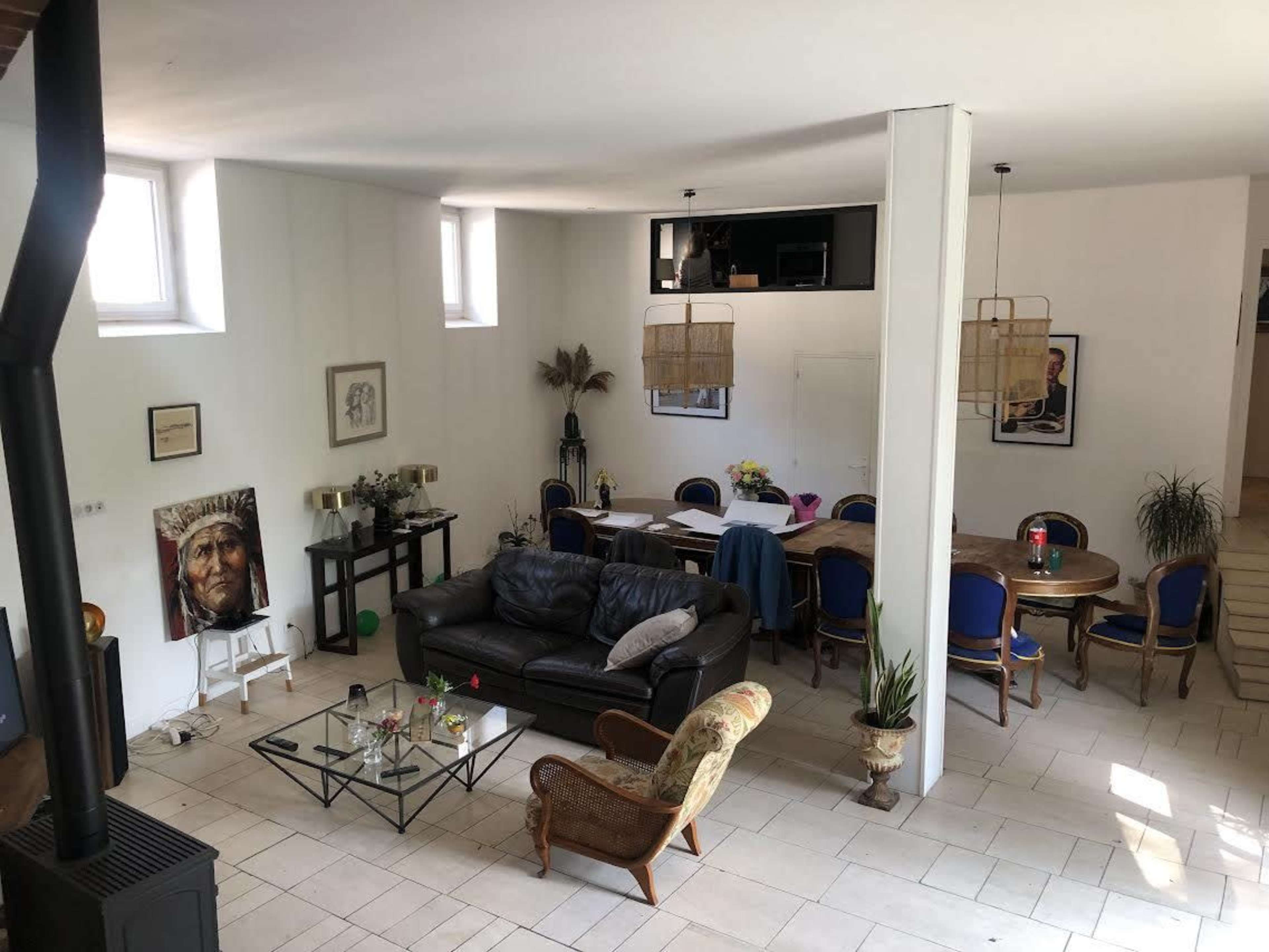 The image shows a spacious living area featuring a couch, coffee table, dining table with chairs, and decorated walls with various artworks.