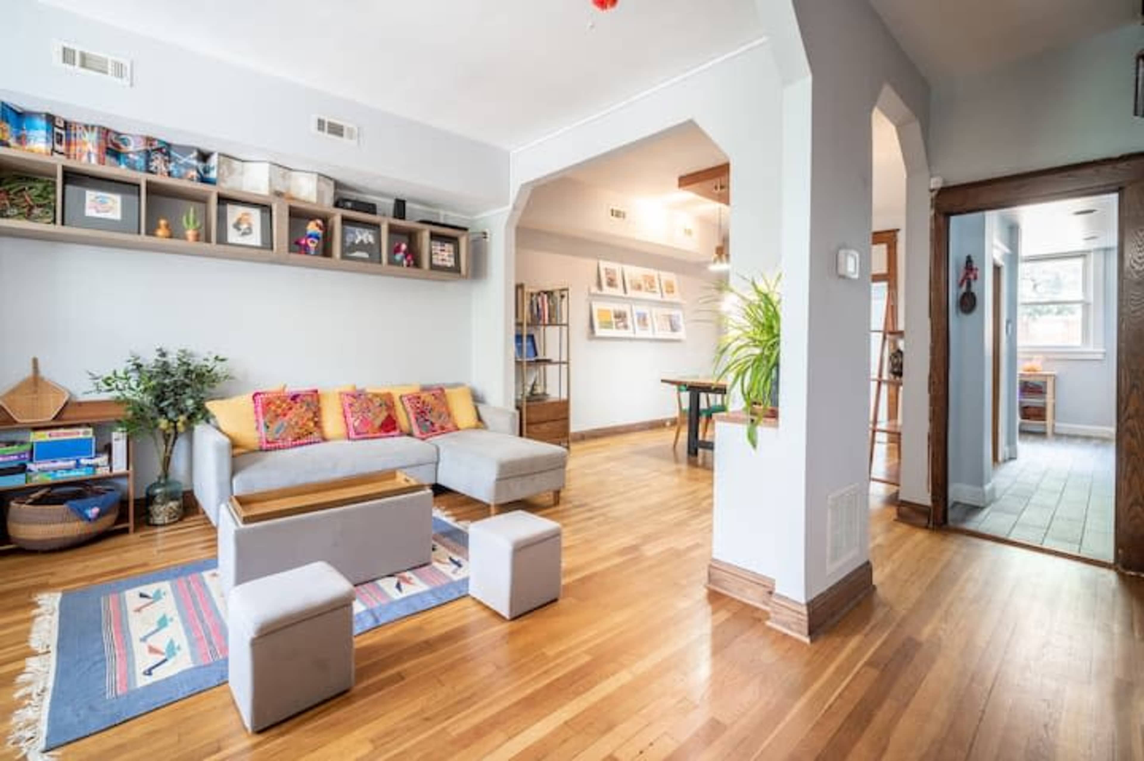 A cozy living room with a gray sofa, wooden floors, and a small coffee table, leading into a hallway and another room.
