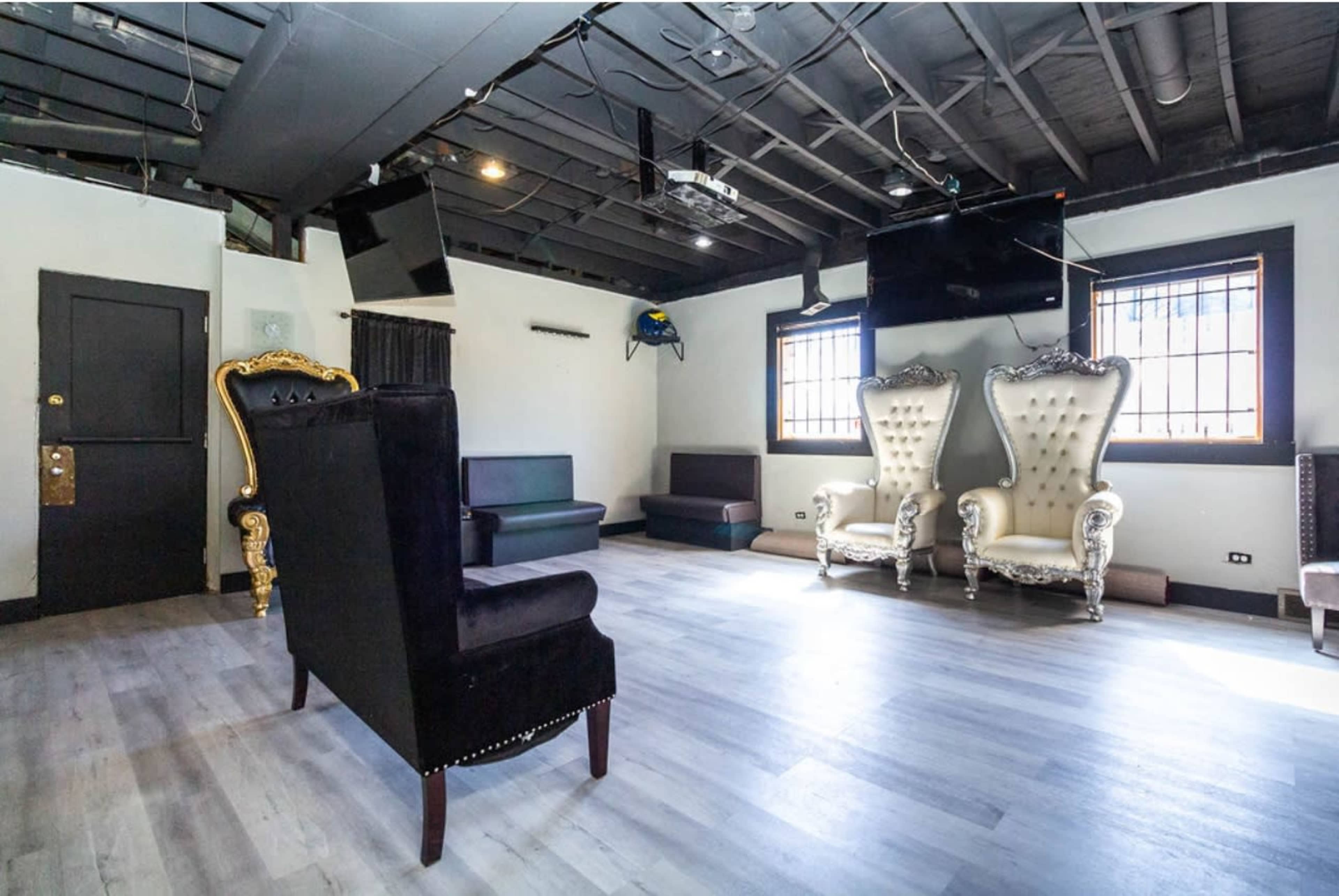 The room features large, ornate chairs and a few couches, with a modern, open layout and exposed beams in the ceiling.