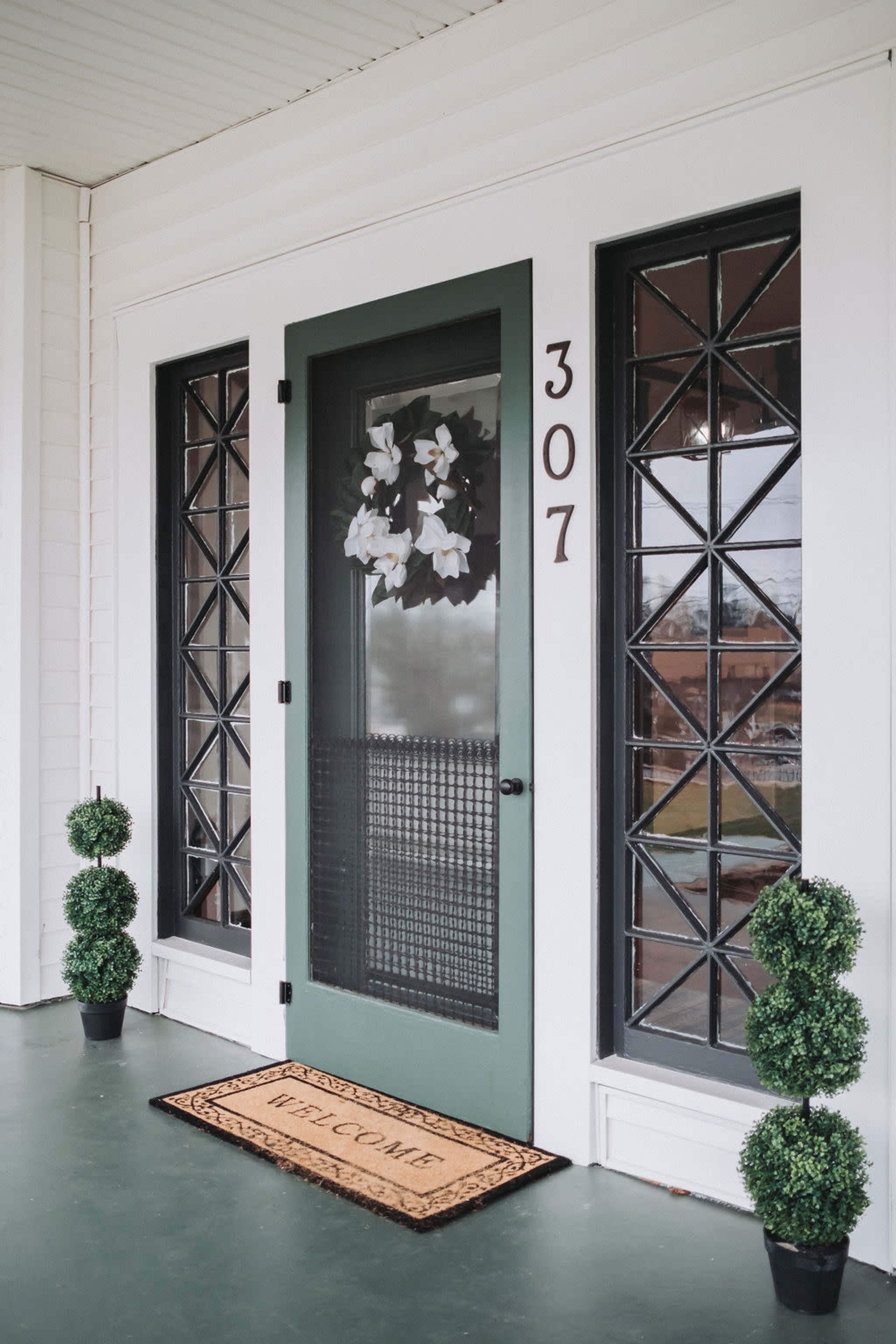 A front porch with a green door, address number 307, two plants on either side, and a welcome mat in front.